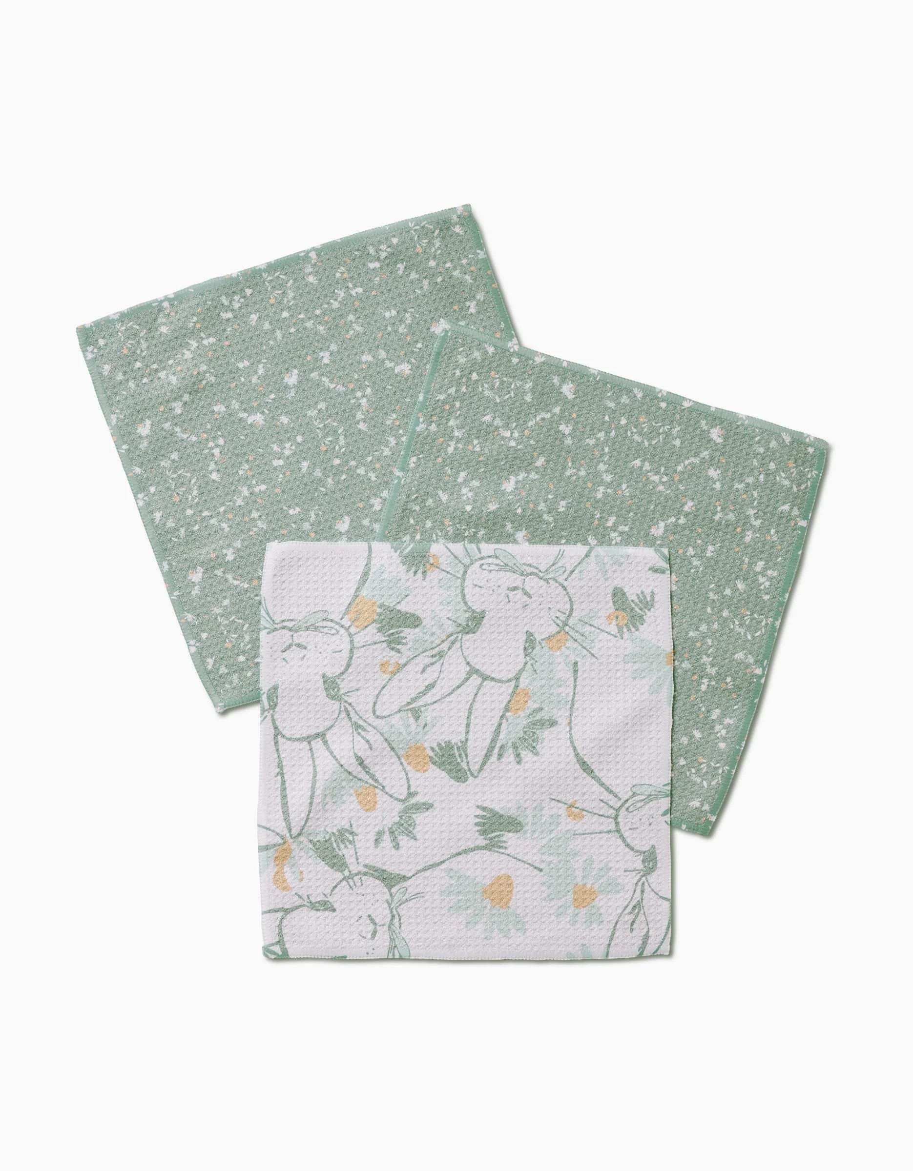 Three Bunny Tea Time dishcloths by Second Nature Studio are shown: two with a green and white speckled Geoweave pattern, and one with a super-absorbent white background featuring carrots and leafy greens.