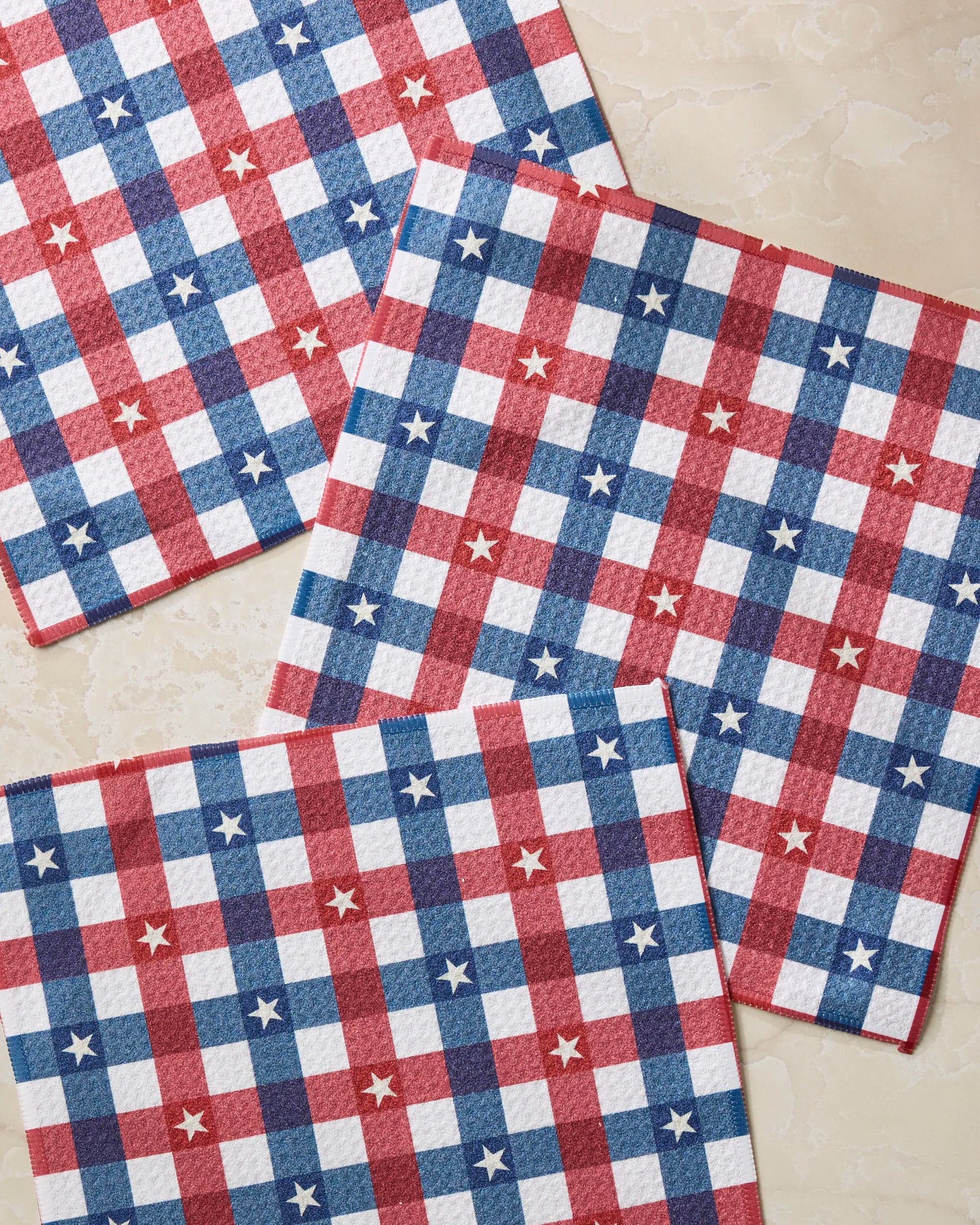 Four Bunting Check paper napkins by Geometry, featuring a red, white, and blue checkered pattern with white stars, are arranged on a light surface to add a festive accent to your table or dishcloth set.