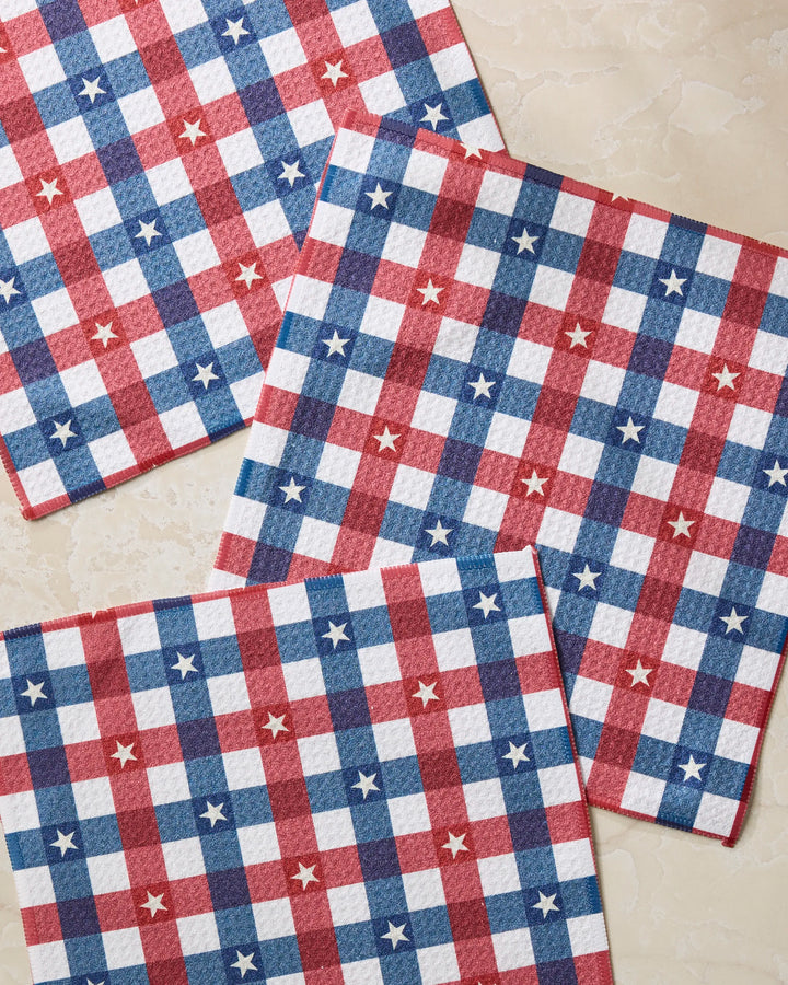 Four Bunting Check paper napkins by Geometry, featuring a red, white, and blue checkered pattern with white stars, are arranged on a light surface to add a festive accent to your table or dishcloth set.