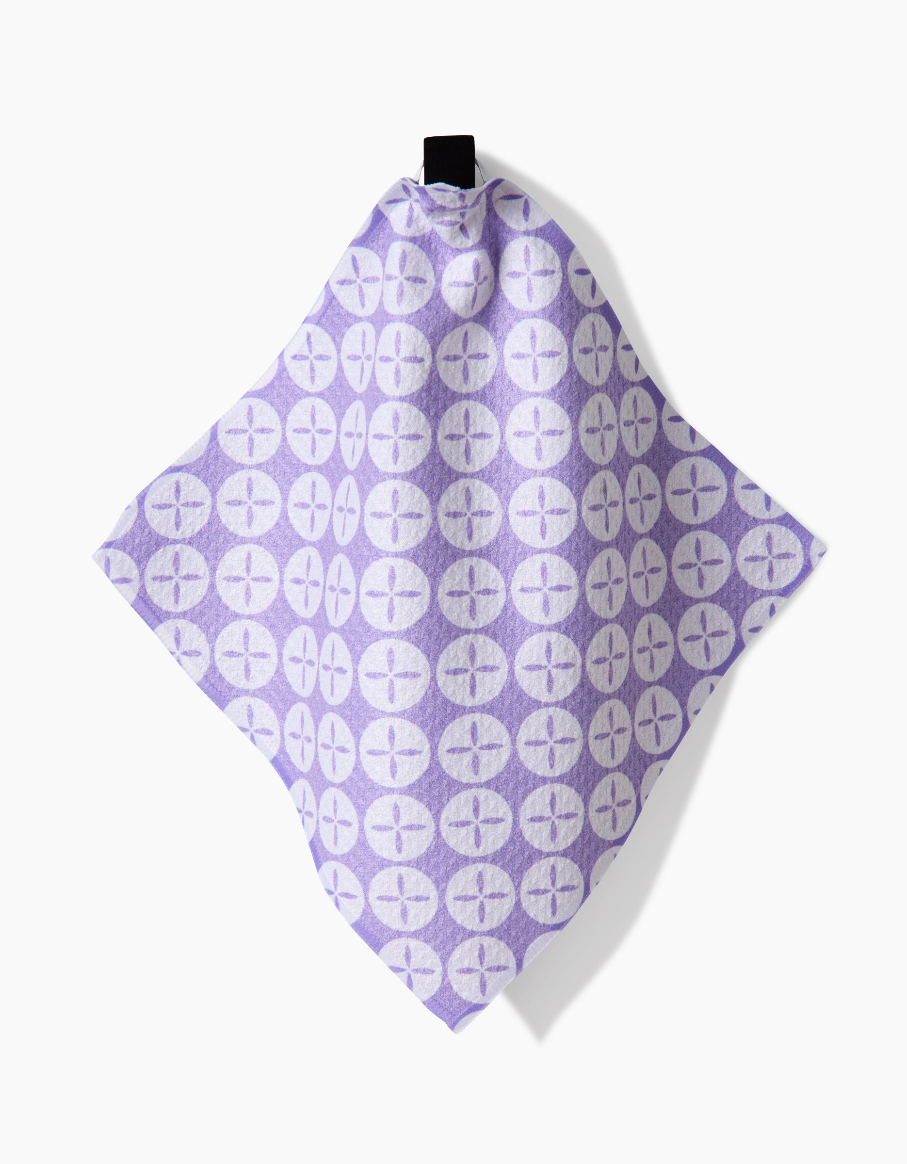 The Button Vines and Daisies towel by Hufton Studio, made from Geoweave fabric, features a lavender hue and a pattern of circular four-petal flowers. It hangs from a black loop against a white background.