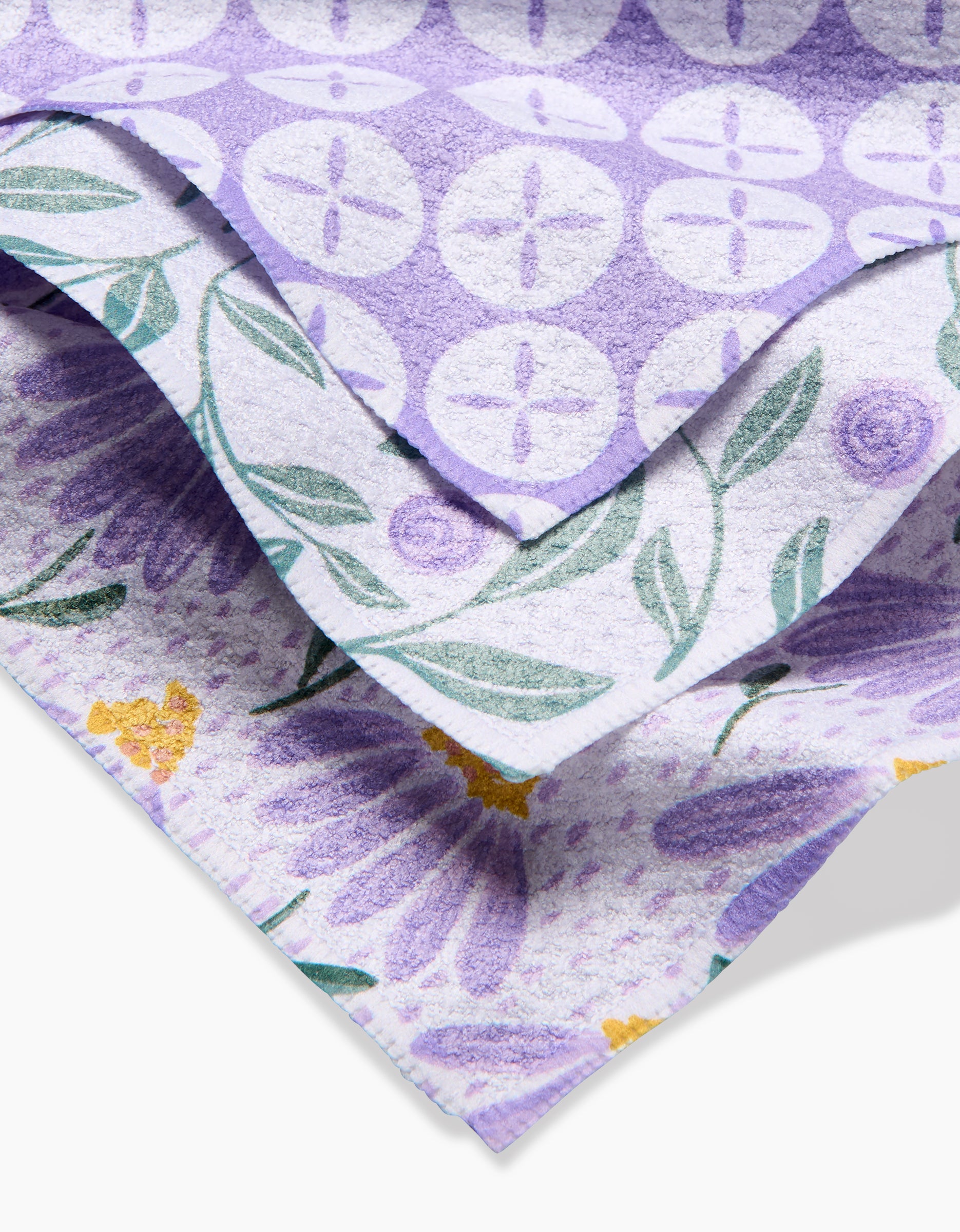 Three stacked Button Vines and Daisies dishcloths by Hufton Studio—purple-themed patterns include white geometric circles, green leaves with purple flowers, and large purple daisies with yellow centers—all made from recycled materials.