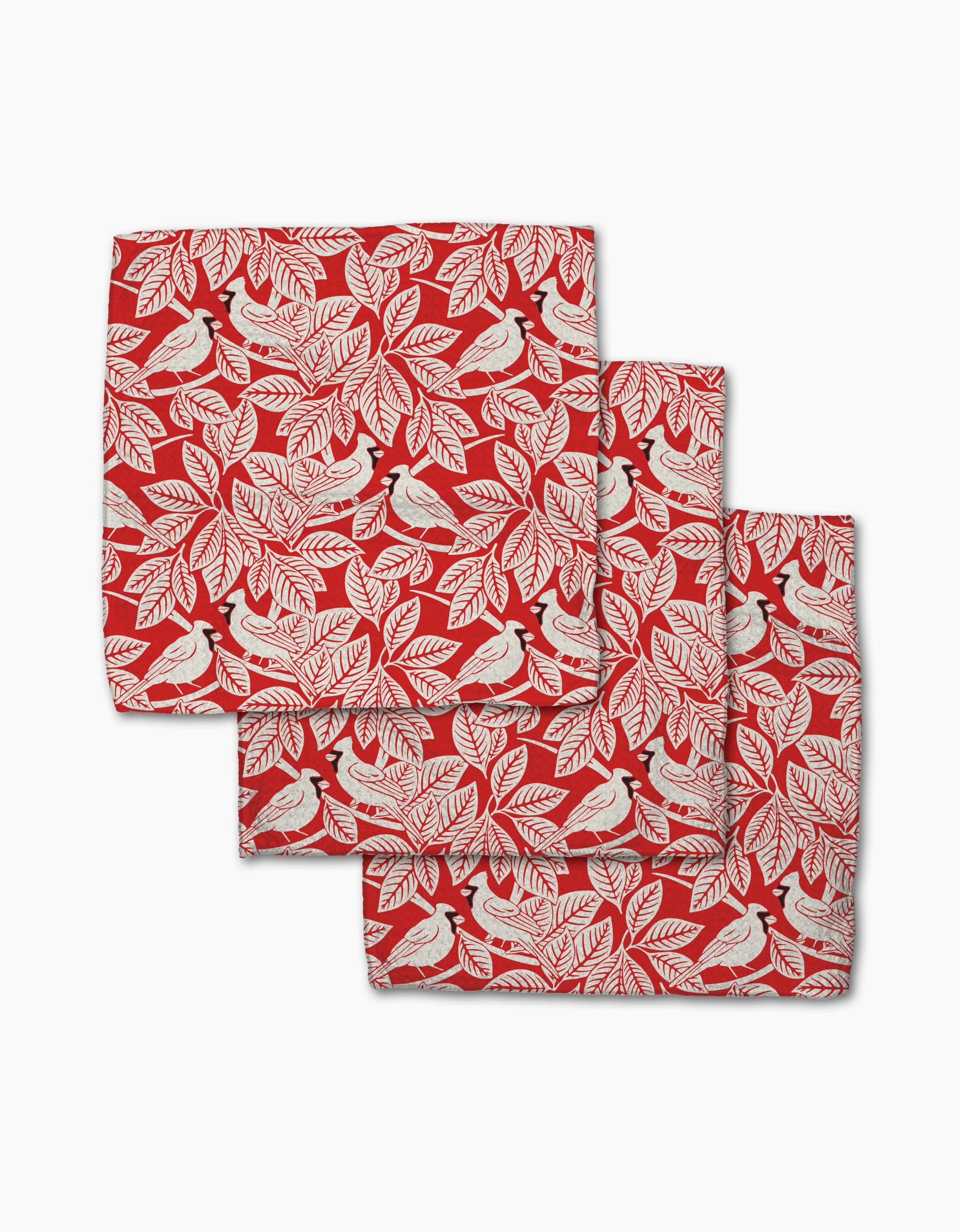Three Cardinal Canopy napkins by Sarah Daugherty, made from recycled materials with a red design featuring white leaves and birds, are neatly stacked with overlapping edges on a white background.