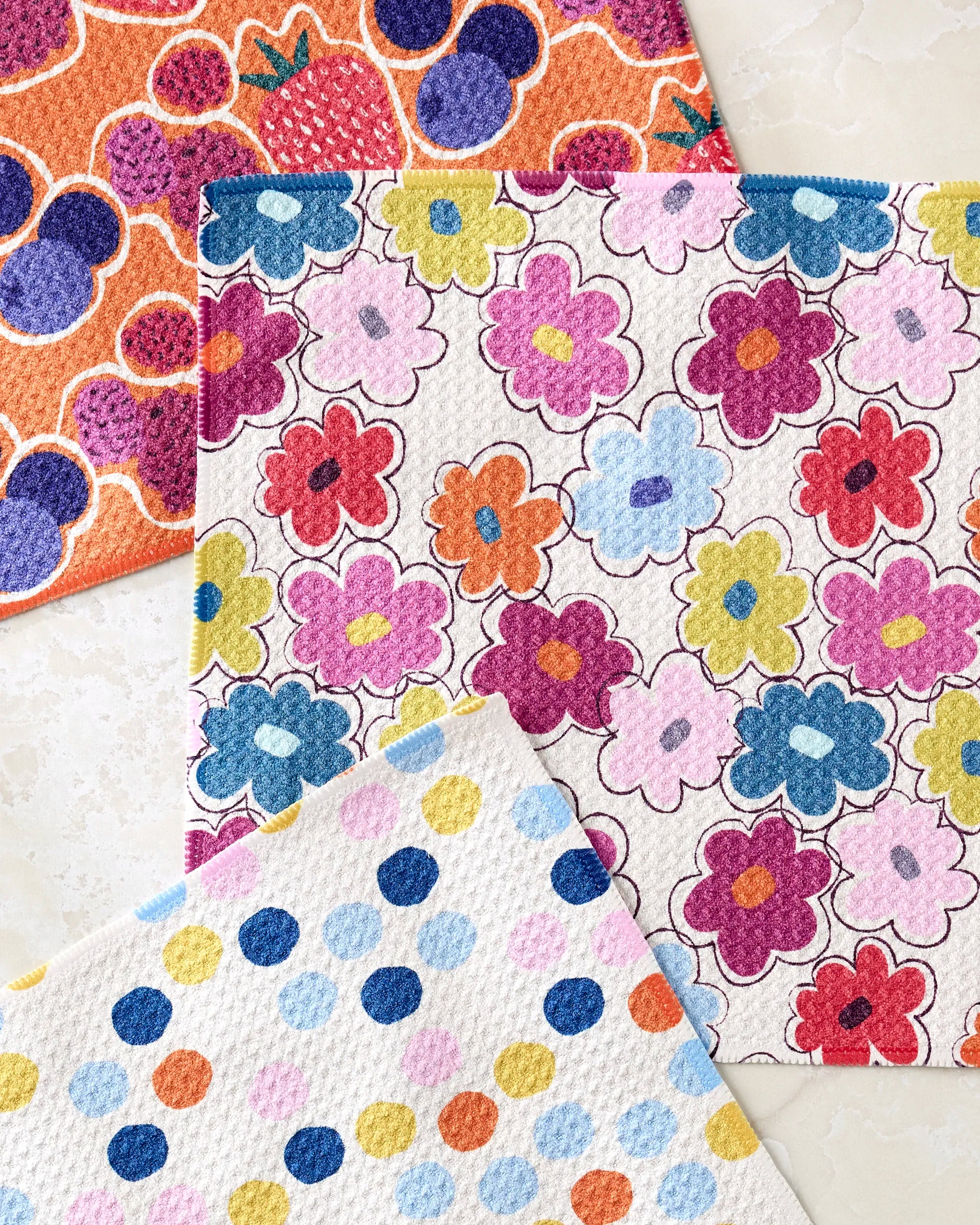 The Carnival Fling set by Lizzie Clark includes three colorful, super-absorbent dishcloths: strawberries & Mickey heads on orange, multicolored flowers on white, and pastel polka dots—perfect for brightening any kitchen.