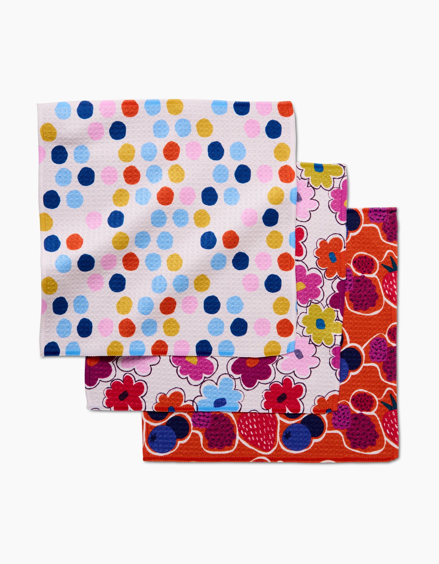 Carnival Fling by Lizzie Clark: three stacked, colorful cloth napkins made from recycled materials—the top with multicolored polka dots on white, the two beneath featuring vibrant floral patterns.