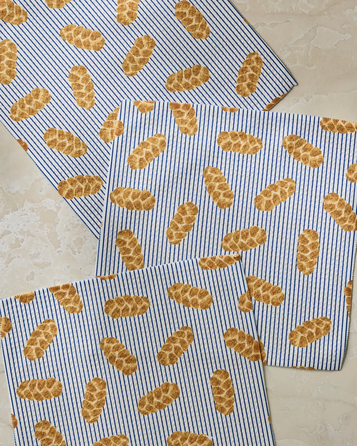 Add a touch of charm and functionality to your kitchen with Geometry’s “Challah Days” dish towel set—three blue-and-white striped towels featuring a delightful repeating pattern of braided challah loaves, perfect for brightening up any light-colored surface.