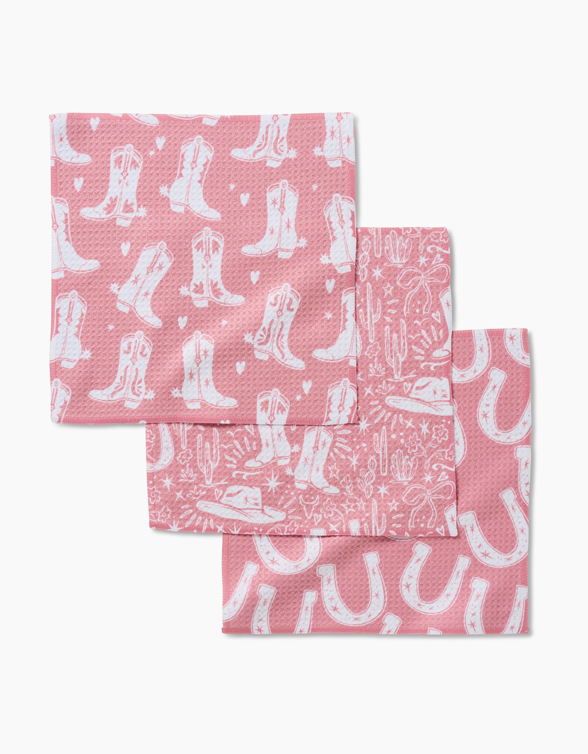 The Chic Lucky Boots set includes three pink kitchen towels made from recycled materials, each with a white Western pattern—cowboy boots, horseshoes, or cacti and stars—neatly stacked in an overlapping display.