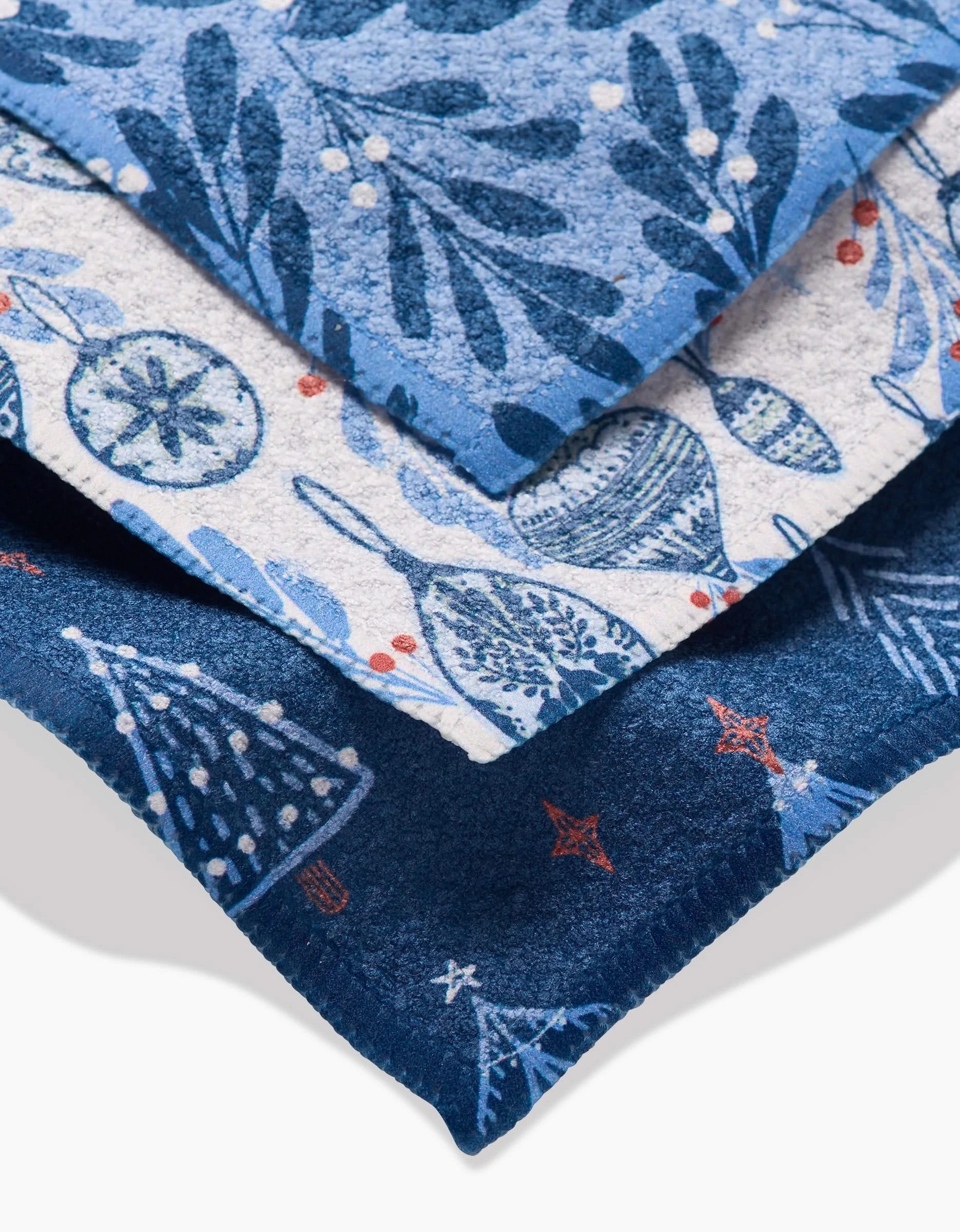 Hufton Studios Christmas Decorations set includes three stacked blue dishcloths, each with festive holiday patterns like ornaments, foliage, and Christmas trees. Made from Geoweave fabric, they feature cheerful white and red accents.