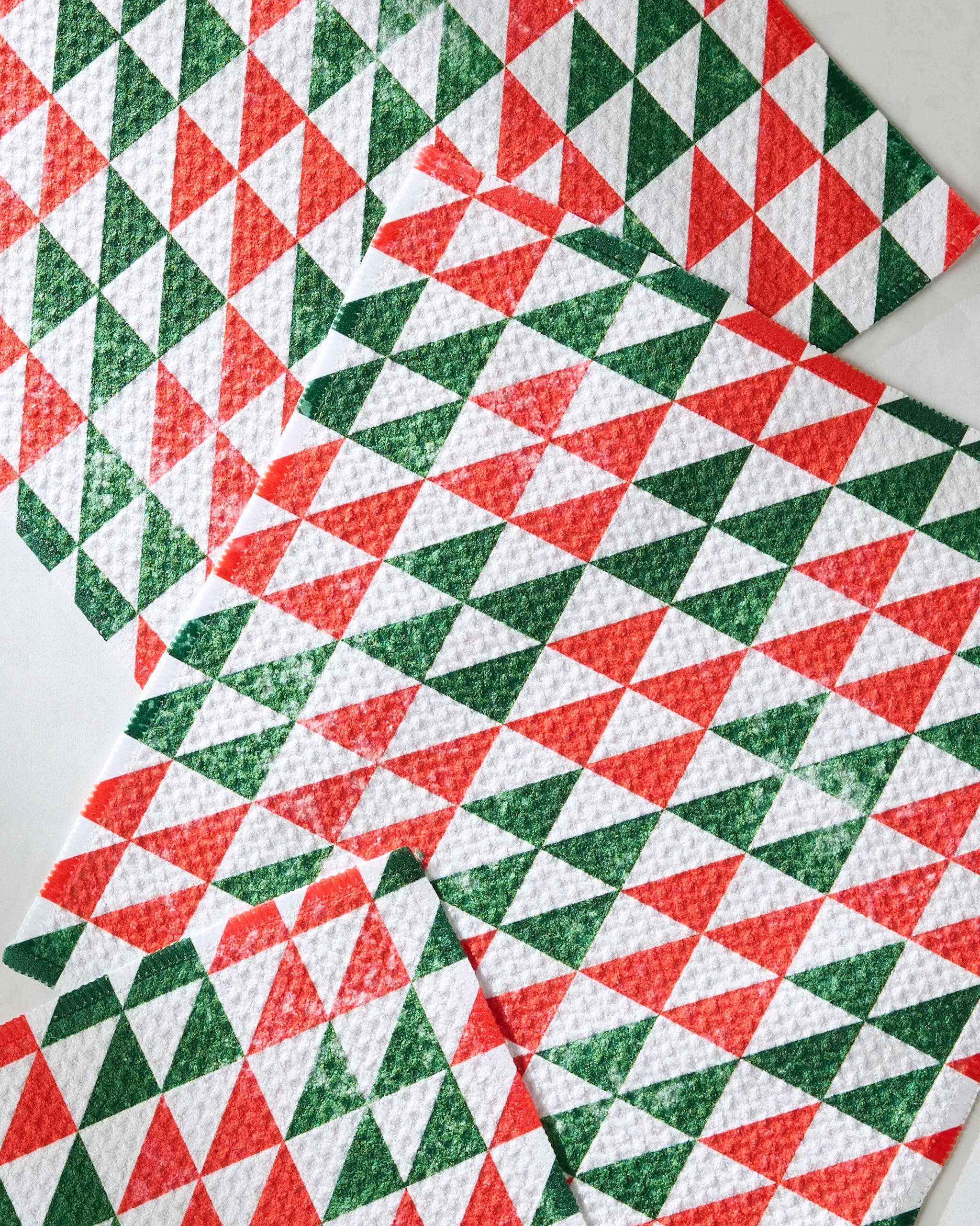 The Christmas Evergreen by Geometry features four overlapping cloths made from recycled materials, showcasing a festive red, green, and white geometric triangle pattern.