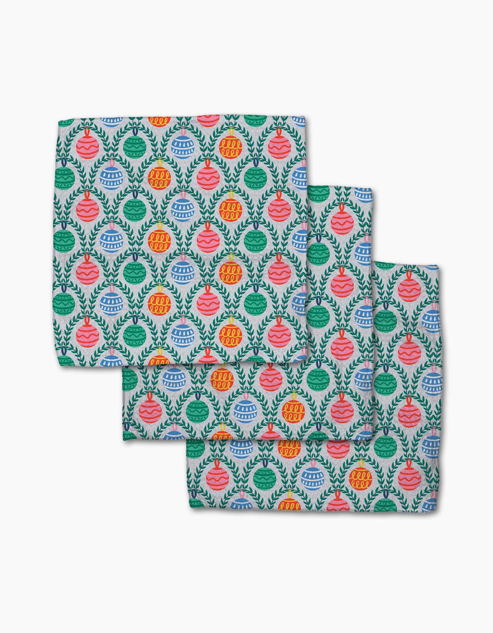Ceyda Alasar's Christmas Ornaments set includes three folded fabric napkins made from recycled materials, featuring a repeating pattern of colorful ornaments and leafy branches on a white background.