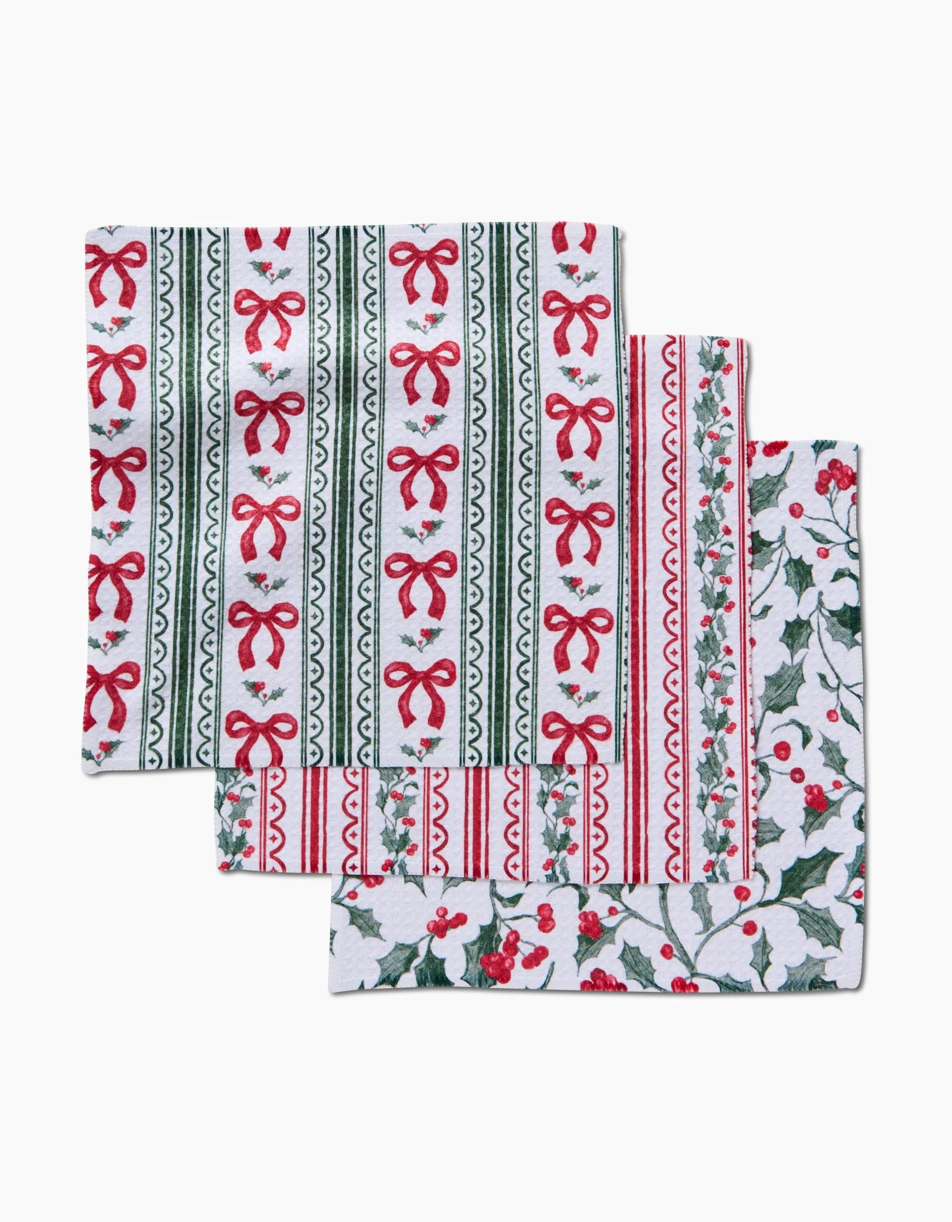 The Aubrey Fairchild Christmas Ribbons set includes three festive Geoweave cloth napkins: two with red bows, green stripes, and holly patterns, plus one with holly leaves and red berries on white.
