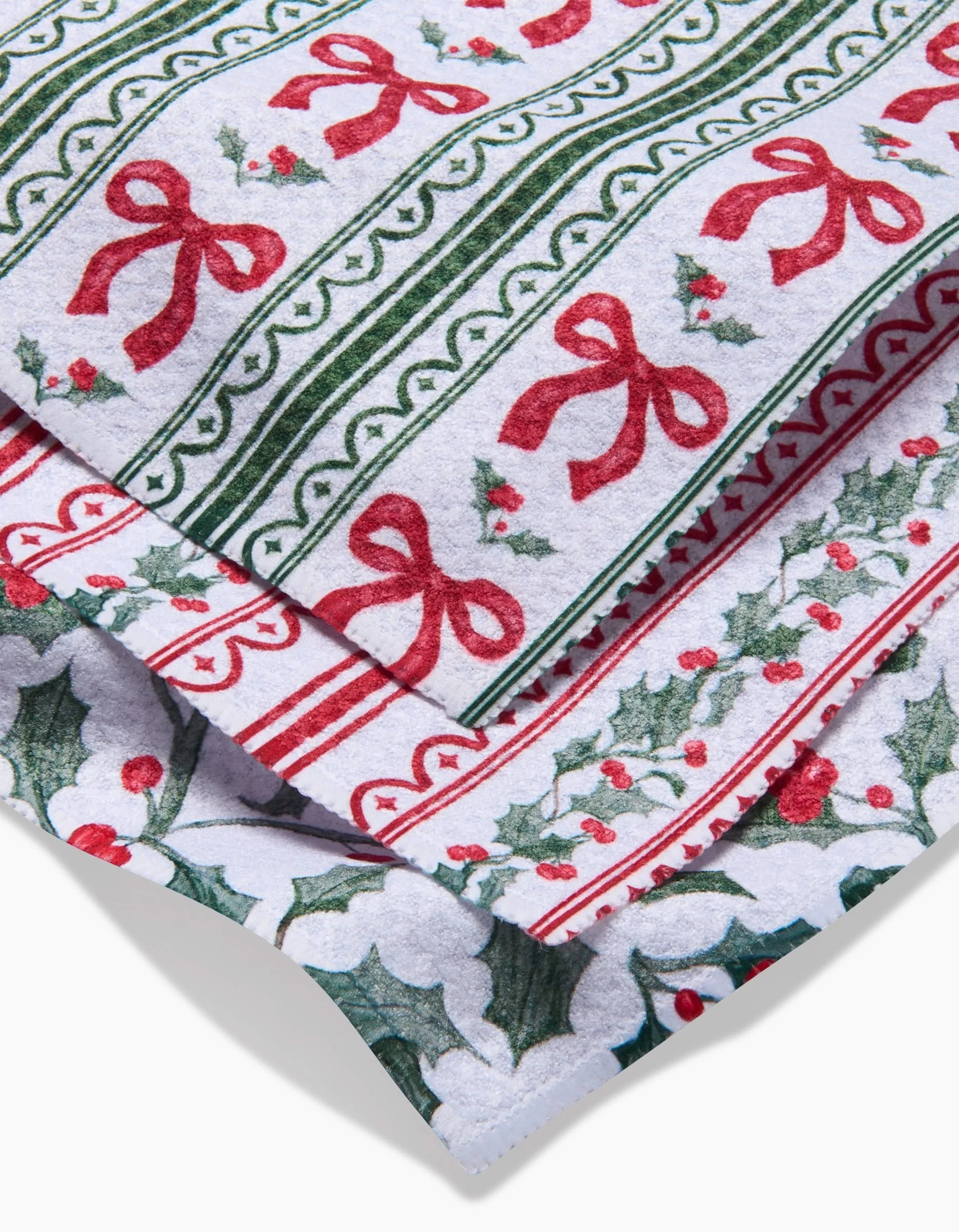 Close-up of Aubrey Fairchilds Christmas Ribbons Geoweave dishcloth, featuring super-absorbent fabric with vibrant red bows, green stripes, and holly on white in a festive holiday-themed design.