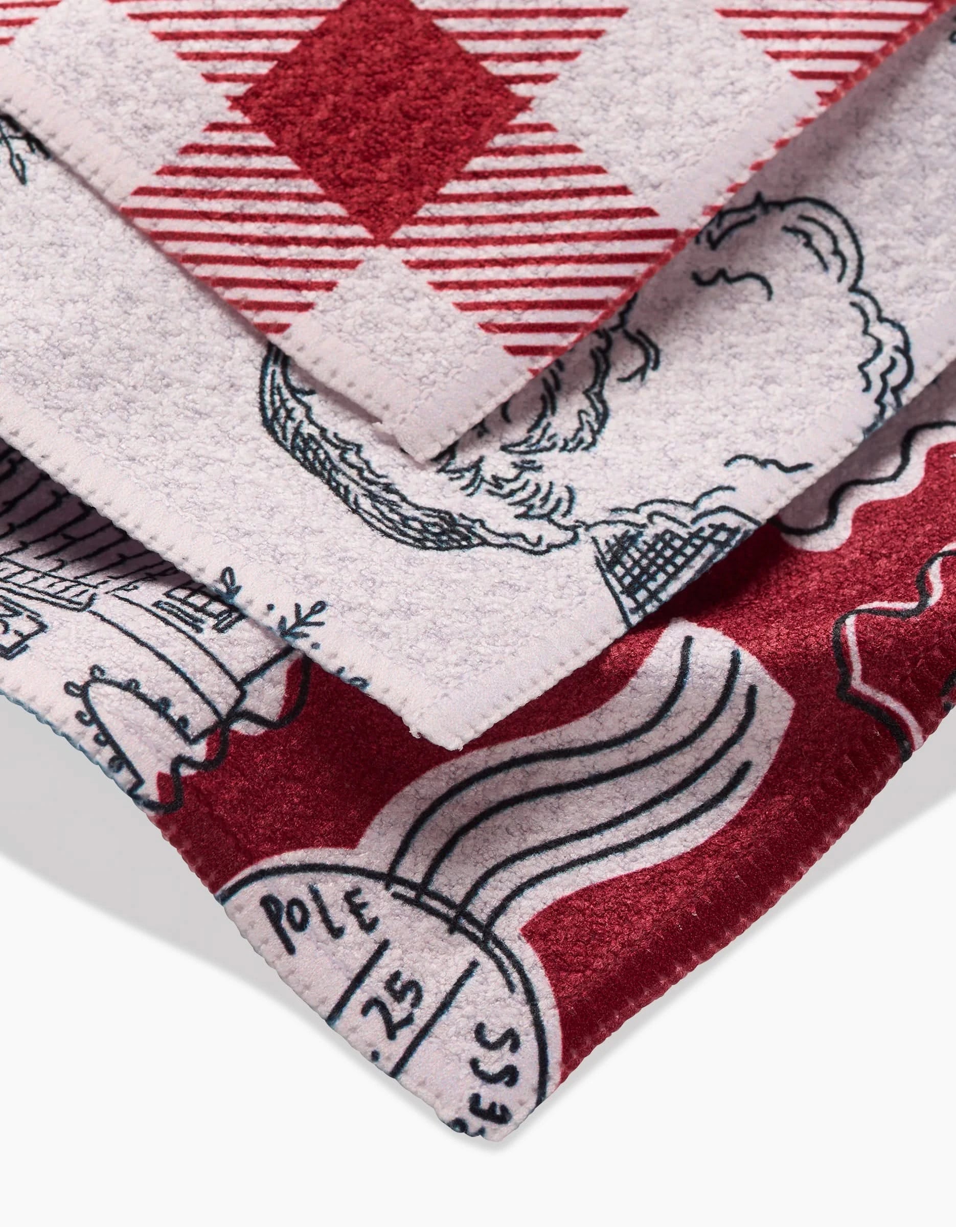 A close-up of three stacked towels from Aubrey Fairchilds Christmas Santa line displays rich texture and detail, featuring festive red, white, and black designs—possibly crafted from recycled materials.