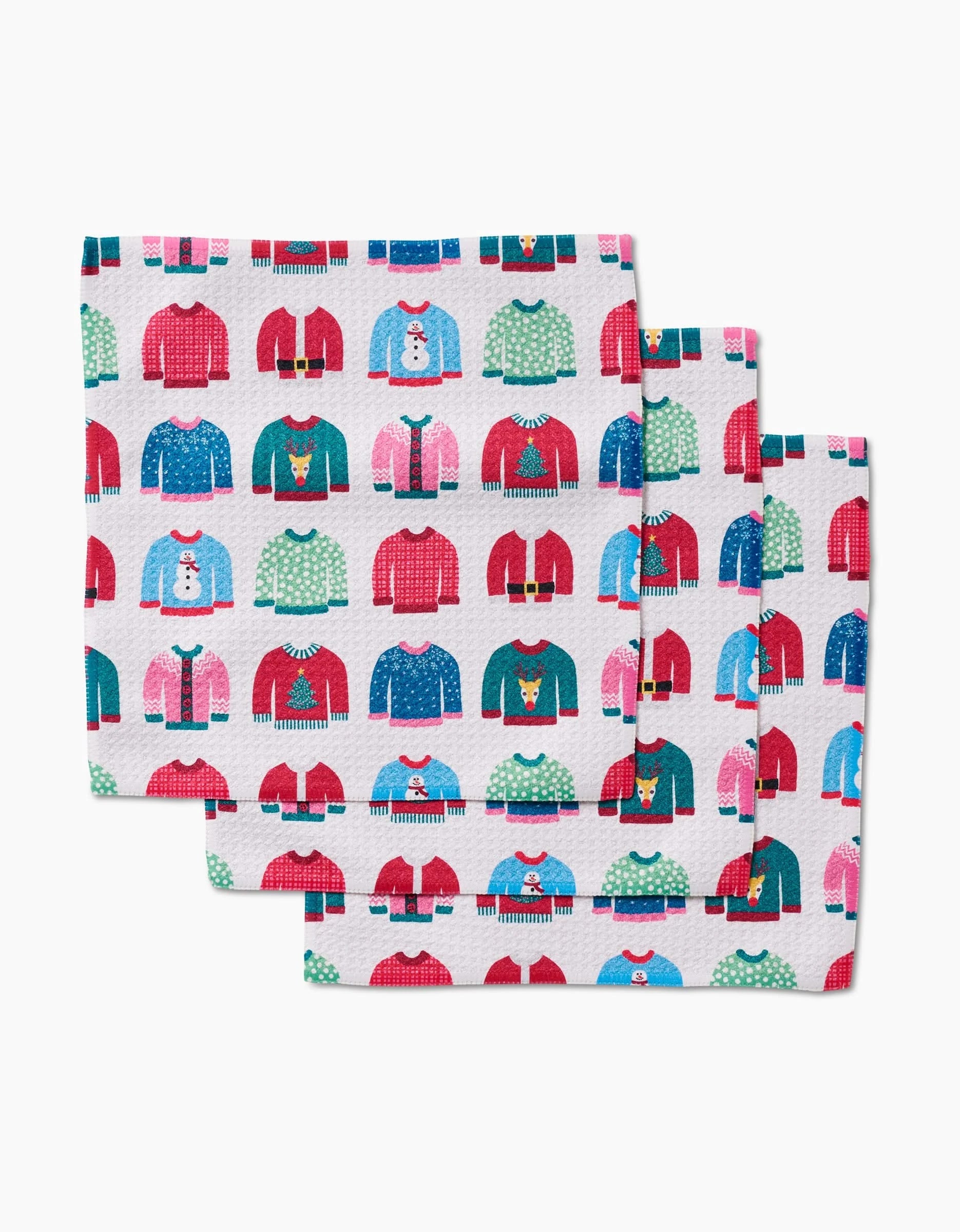 Rebecca Bobko’s “Christmas Sweaters” features three stacked napkins made from recycled materials, adorned with a festive pattern of holiday sweaters in red, blue, green, and pink on a white background.
