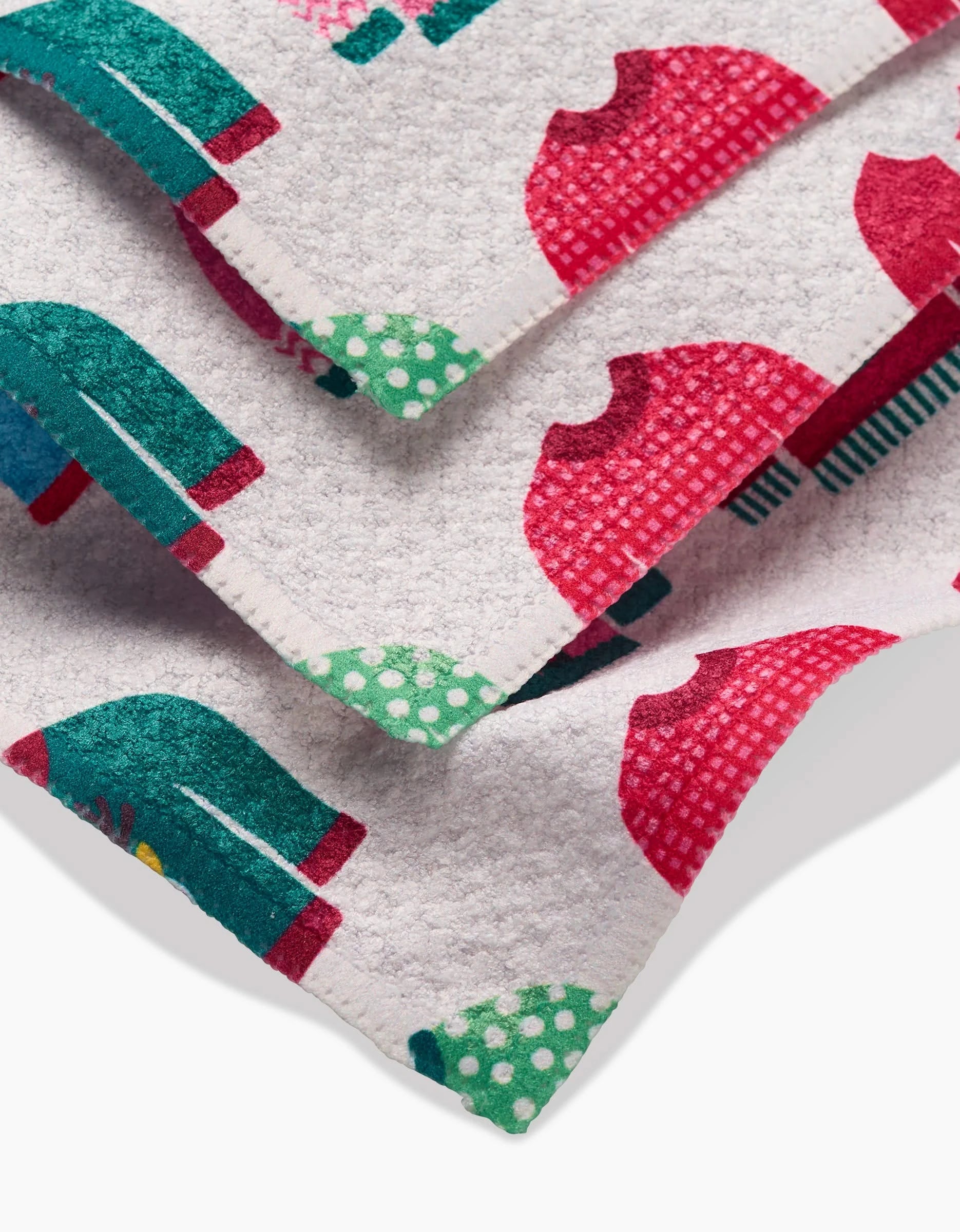 Three overlapping Christmas Sweaters Geoweave dishcloths by Rebecca Bobko, with a white base and colorful red and green sweater and polka dot patterns, are displayed on a flat surface.