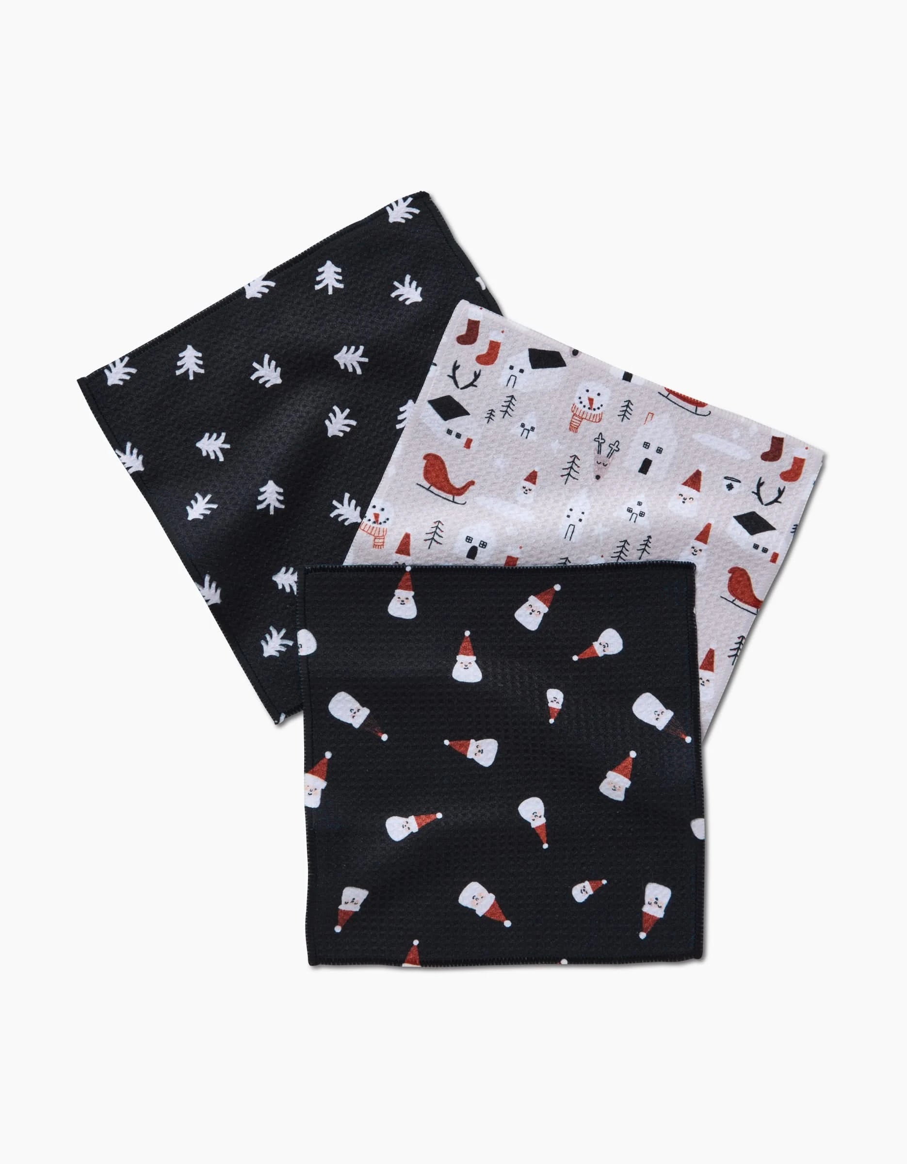 Set of three Christmas Village napkins by Coit Creative: festive prints on super-absorbent Geoweave—black with white trees, white with holiday icons, and black with Santa faces in red hats.