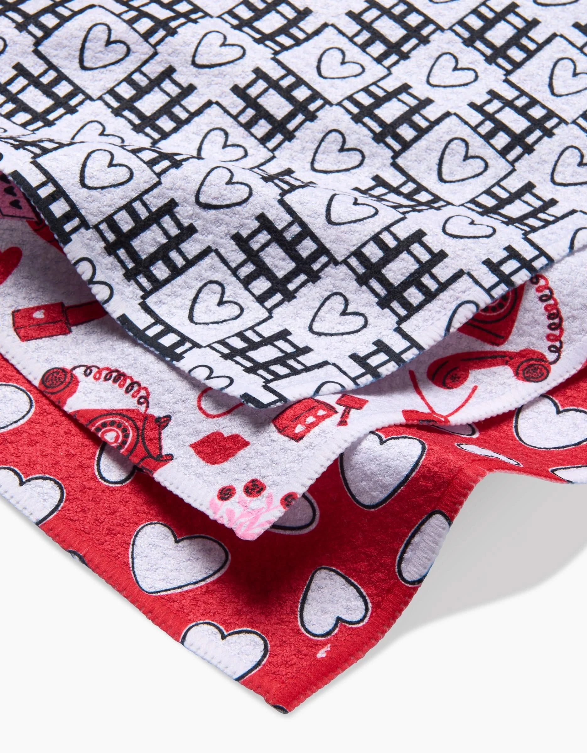 Charlie Rowan Designs Classic Loving set features three overlapping dishcloths: white with black hearts and grid, white with red hearts and shapes, and red with white hearts—an adorable, super-absorbent collection.