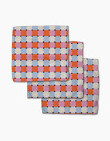 The Claire Iglesias Color Block Grid dishcloth set features three folded, checkered blankets in red, pink, blue, and white. Overlapping on a white background, they highlight fast-drying and super-absorbent qualities—perfect for any kitchen.