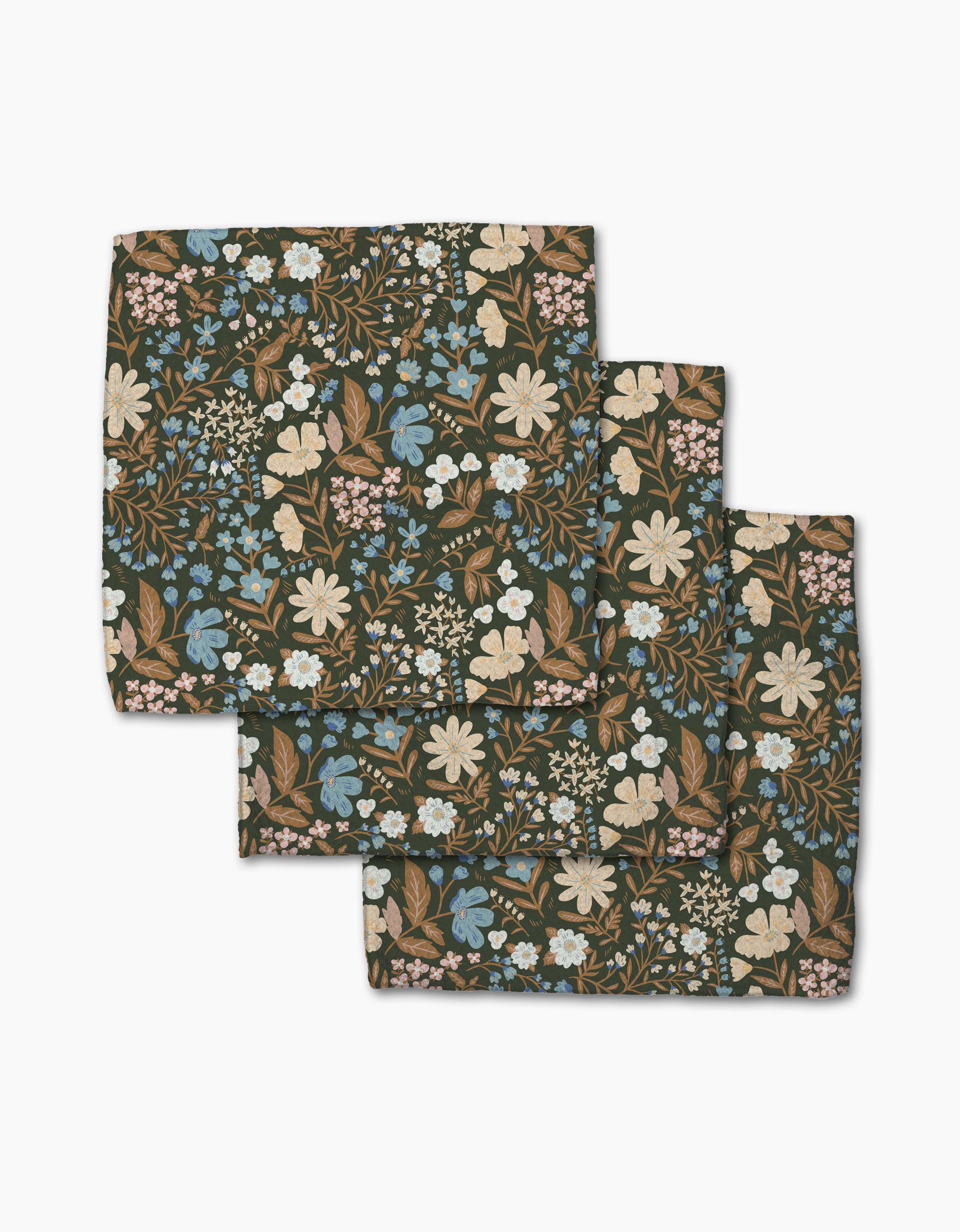 Three folded Cottage Meadow Sepia cloth napkins from Danelys Sidron, made of Geoweave fabric with a floral print in white, blue, and beige flowers plus green leaves on a dark background, are arranged in a layered stack.