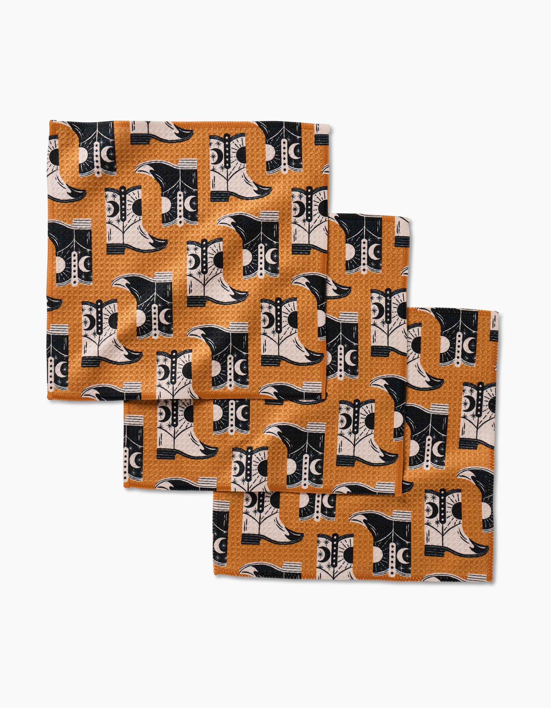 Four square napkins by Megan Roy, called Cowboy Boots, made from Geoweave fabric and featuring a repeating black, white, and orange pattern of cowboy boots, hats, and stars. The set is displayed fanned out on a white background.
