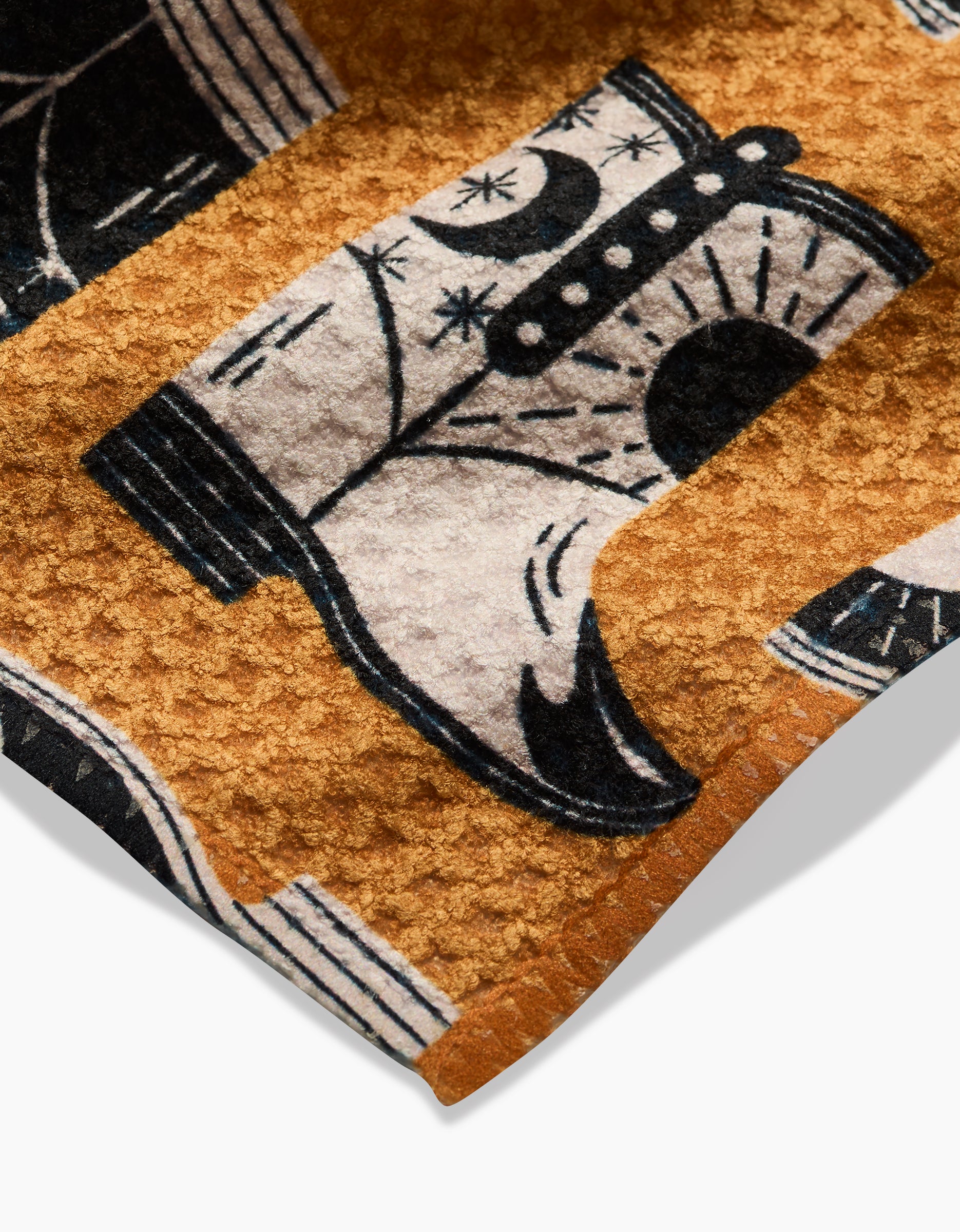 Close-up of Megan Roys Cowboy Boots dishcloth, made from textured Geoweave fabric with a black and white cowboy boot design featuring star and moon details on a warm brown background. Crafted from recycled materials.