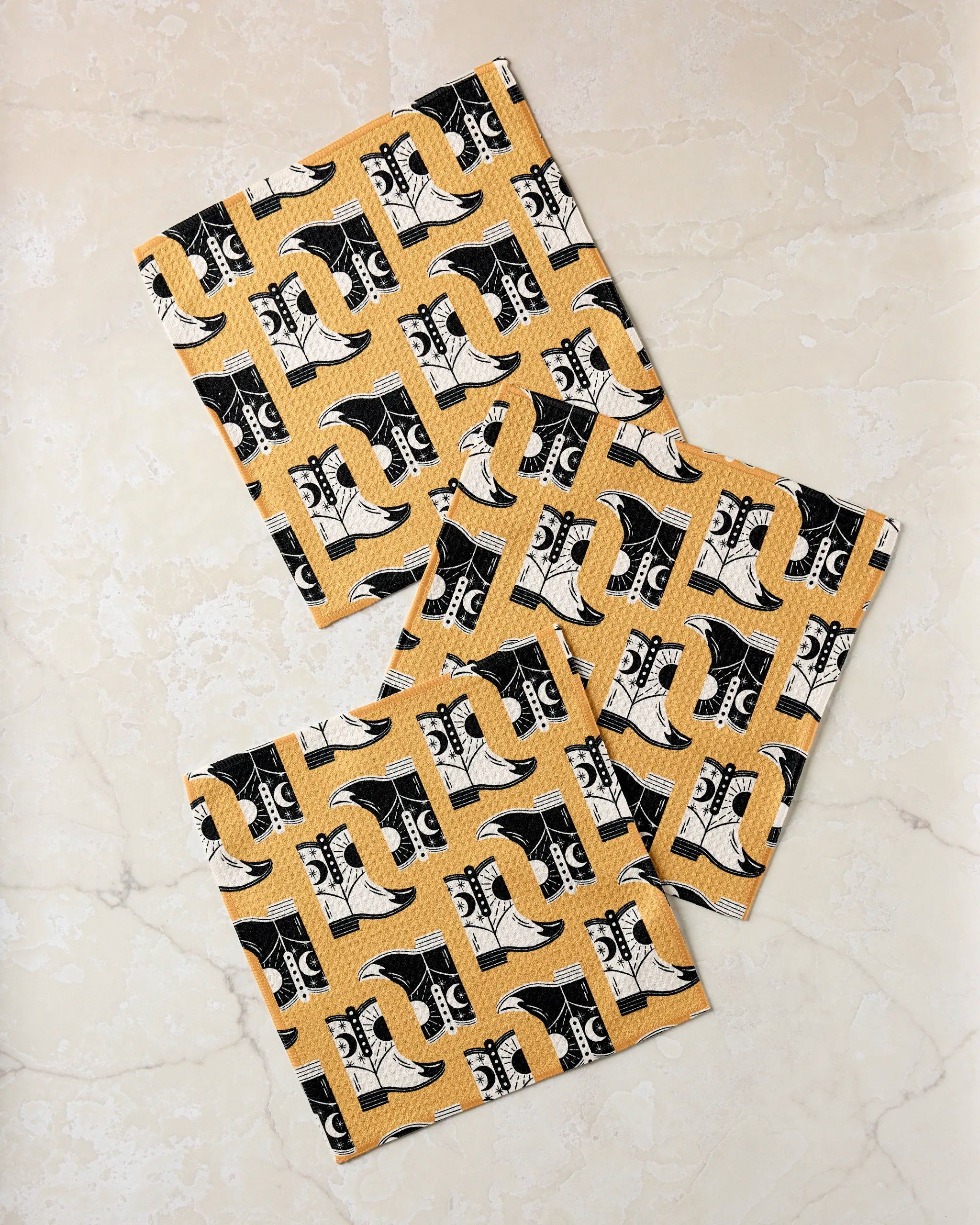 Three Cowboy Boots by Megan Roy are arranged on a light marble surface.