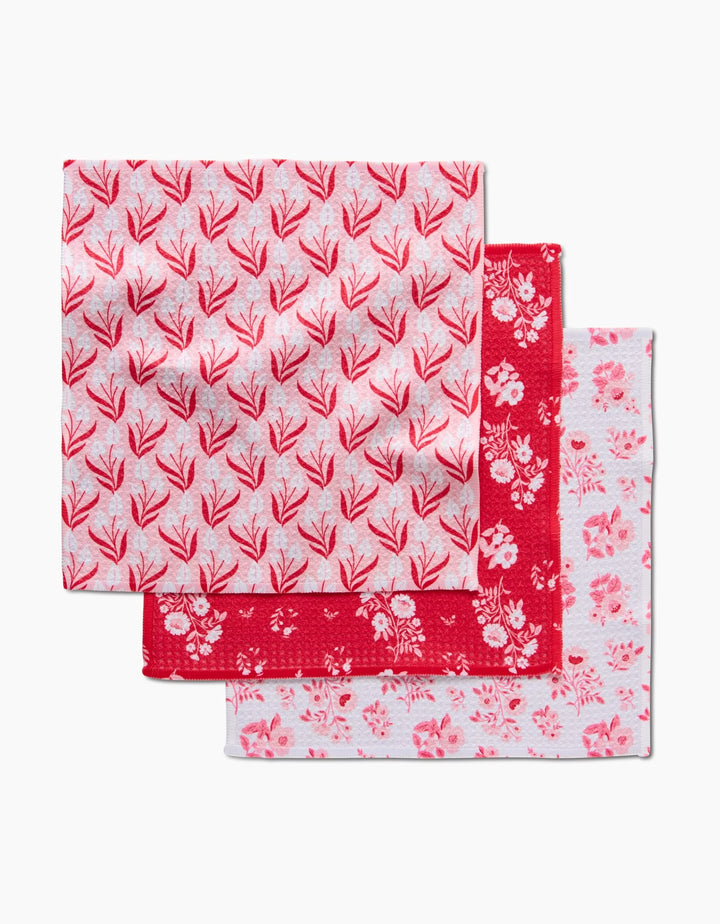 Three square Cupid Garden napkins by Danelys Sidron, each featuring red and pink floral or leaf patterns on white or red backgrounds, crafted from recycled materials and displayed on a white surface.
