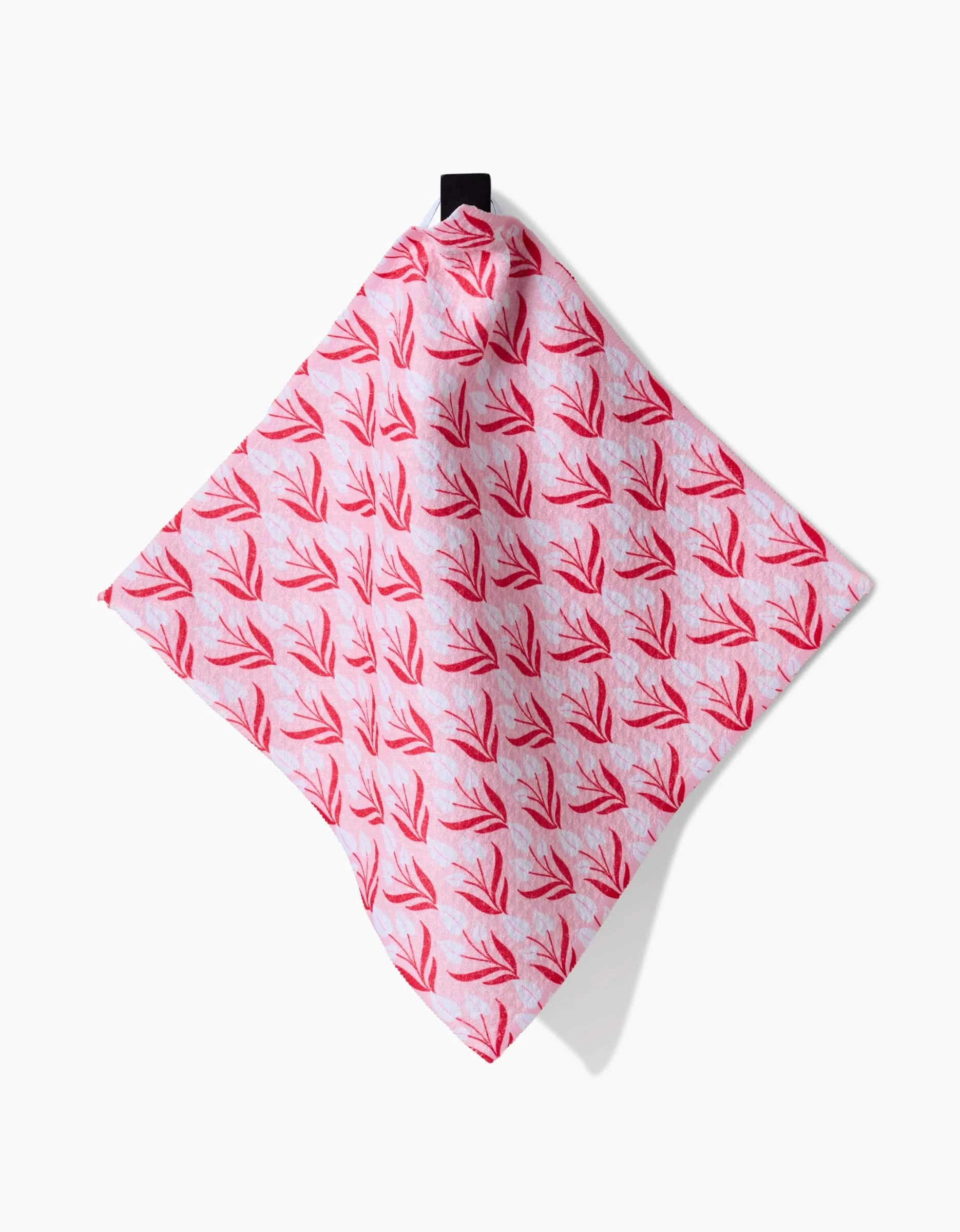 The Cupid Garden dish towel by Danelys Sidron is pink, made from recycled materials, and features a red leaf pattern. It hangs from a black loop against a white background.