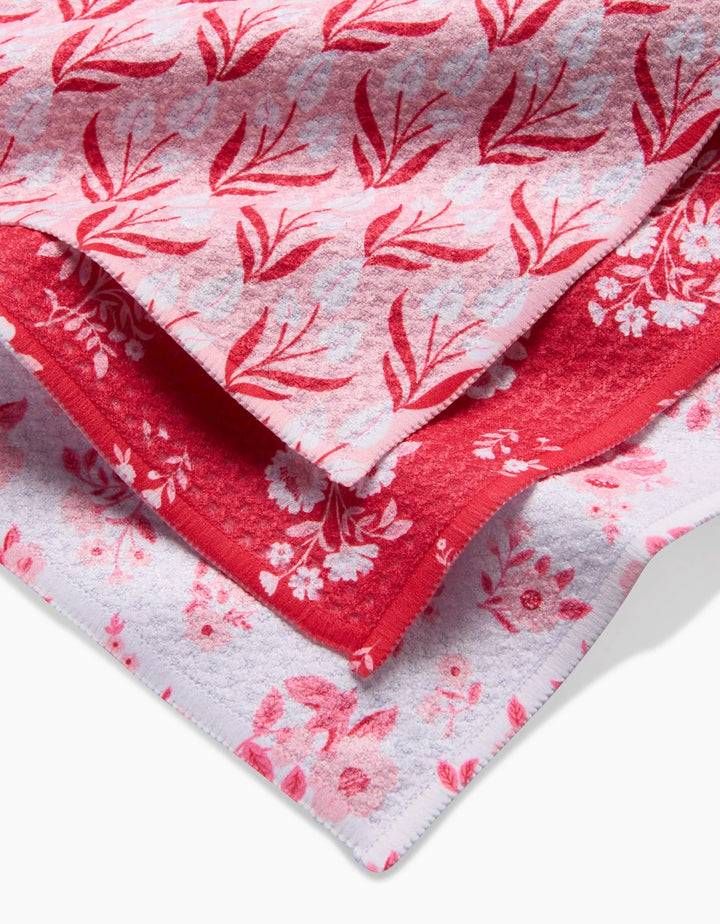 Three overlapping Danelys Sidron Cupid Garden towels made from recycled materials, featuring red and pink floral patterns on white and red backgrounds, shown close up to showcase the unique designs and textures.