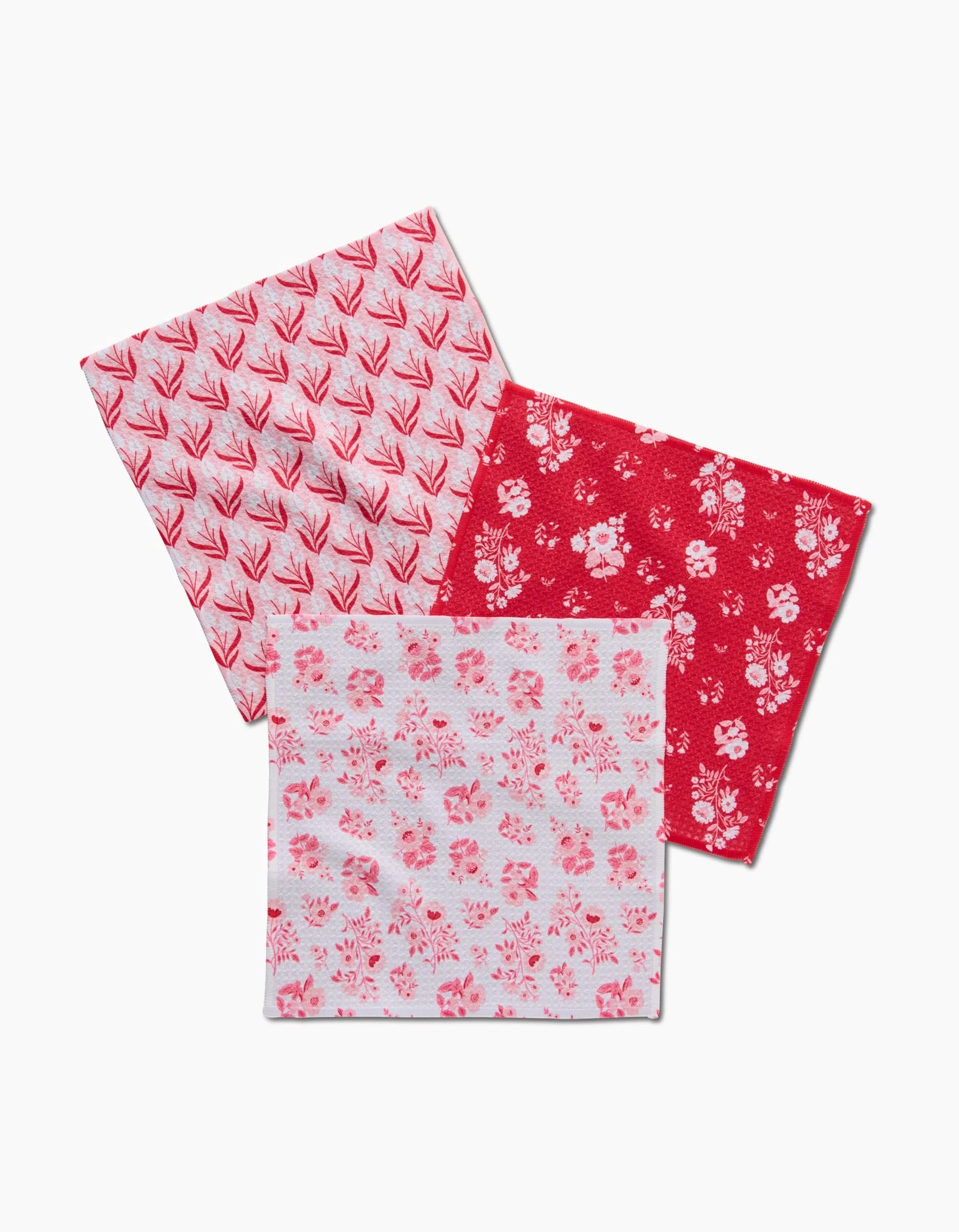 Three square handkerchiefs from Danelys Sidron’s Cupid Garden, each with a unique red and white floral design, are displayed overlapping on a white background—an eco-friendly dishcloth set made from recycled materials.