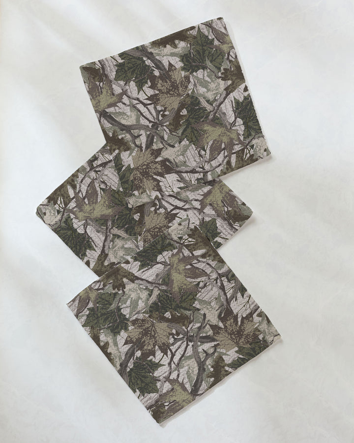 A rectangular piece of Dad Camo fabric by Geometry, featuring a brown, green, and gray camouflage pattern made from recycled materials, is arranged in a zigzag shape on a white surface.