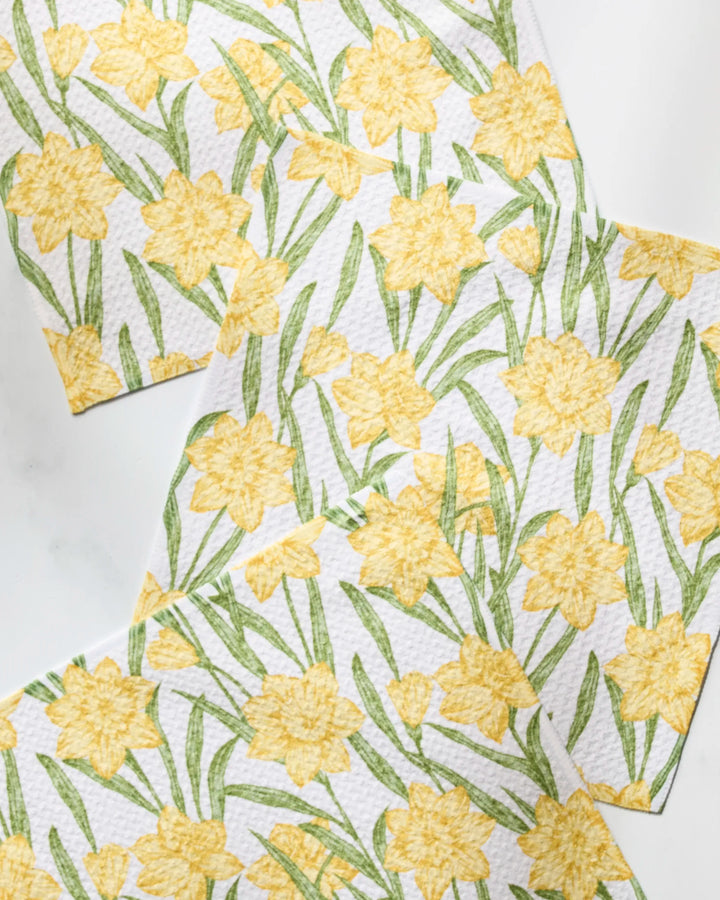 Geometry’s Daffodil Darling set includes four recycled paper napkins, each featuring yellow daffodils and green leaves in a staggered, overlapping design on a white background.