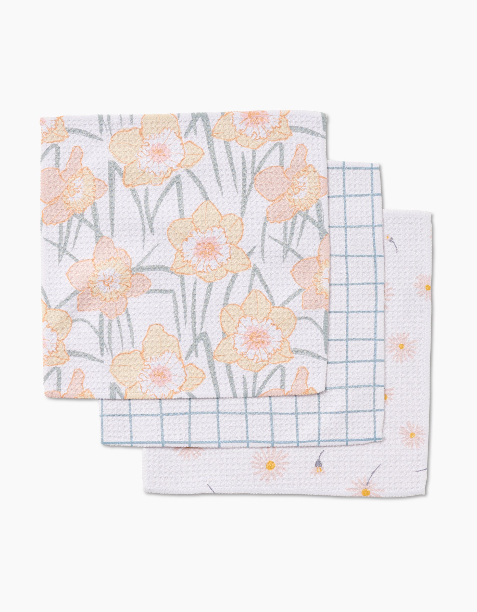 Three folded Hufton Studio Daisy Dust dishcloths are stacked: the top shows a yellow daffodil pattern, the middle a blue grid, and the bottom small yellow flowers—all made from super-absorbent Geoweave fabric.
