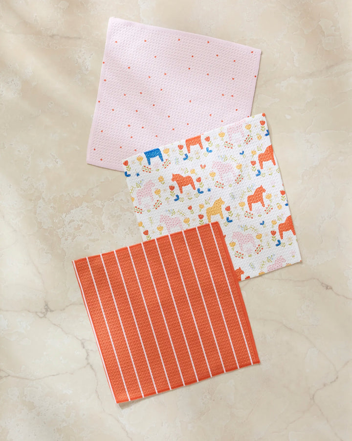 The Sara Mari Dala Garden Floral set features three super-absorbent dishcloths: light pink with dots, white with colorful floral and animal prints, and orange with white stripes.