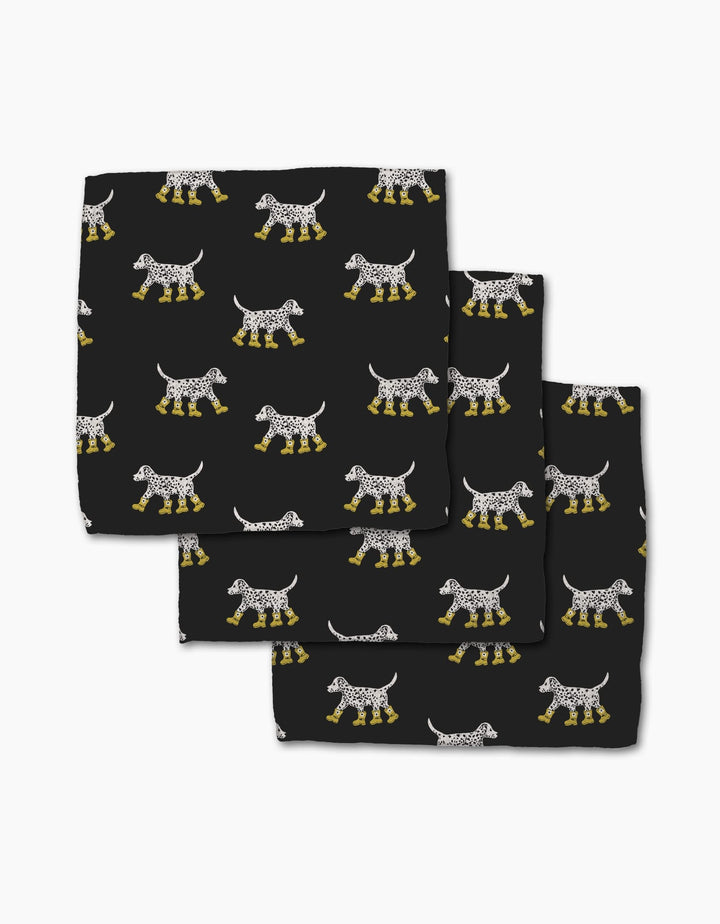 Three folded black Dalmatian In Boots cloth napkins by Geometry, made from recycled materials, display a repeating pattern of white-spotted Dalmatian dogs in yellow boots.