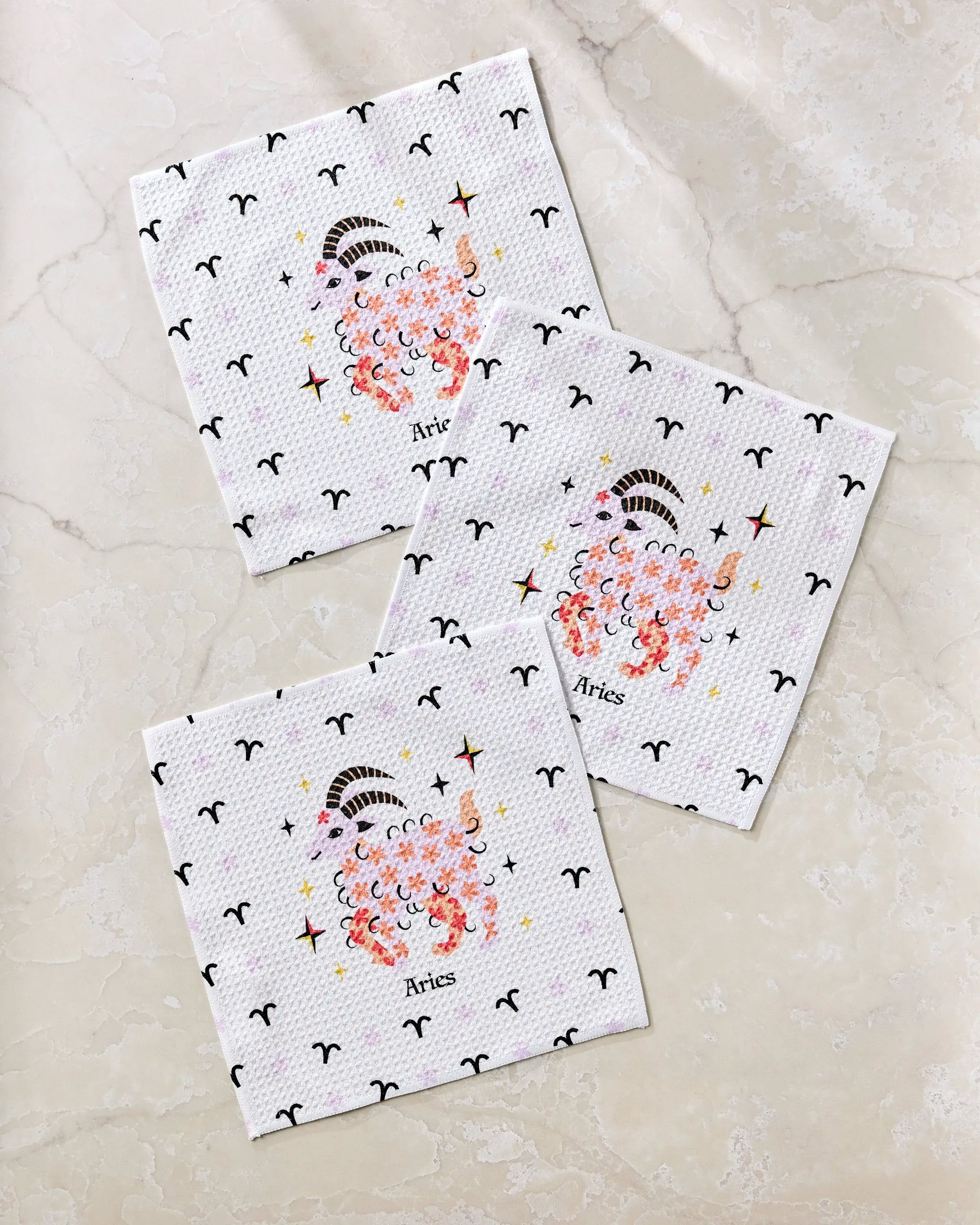 The Daring Aries dishcloth set by Heather Zhou includes three decorative white napkins, each featuring a stylized ram and scattered Aries symbols, perfect for adding zodiac charm to your table.