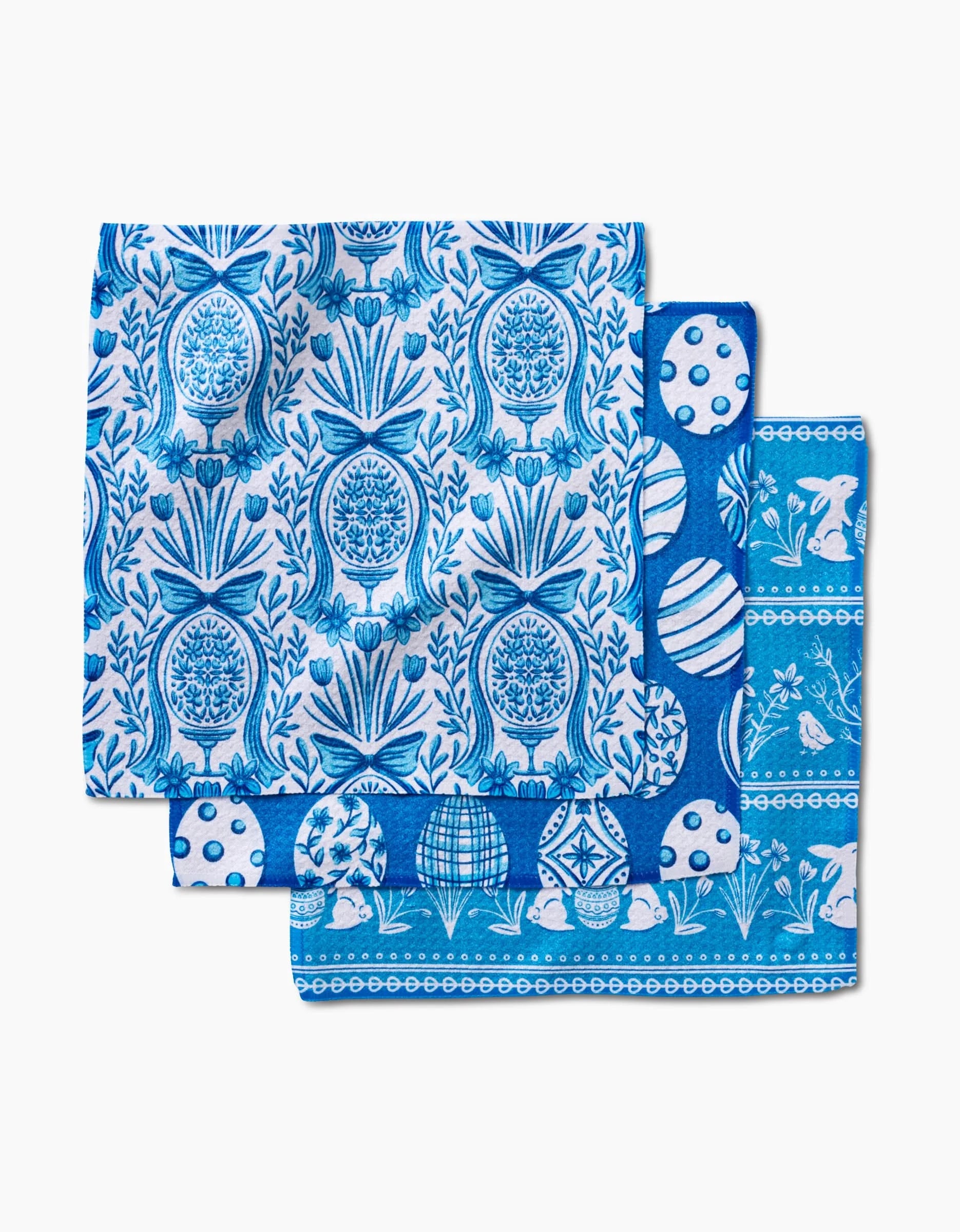 Three Delft Blue Easter Eggs and Bunnies handkerchiefs by Sarah Daugherty, each with unique botanical and geometric patterns, are stacked and partially overlapping on a white background, crafted from recycled materials.