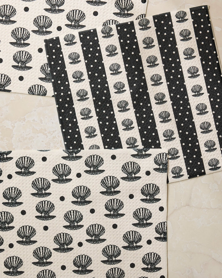 The Geometry Disco Pearls dishcloth set features black seashell designs and alternating black and white polka dot stripes, crafted from recycled materials and showcased on a light marble surface.