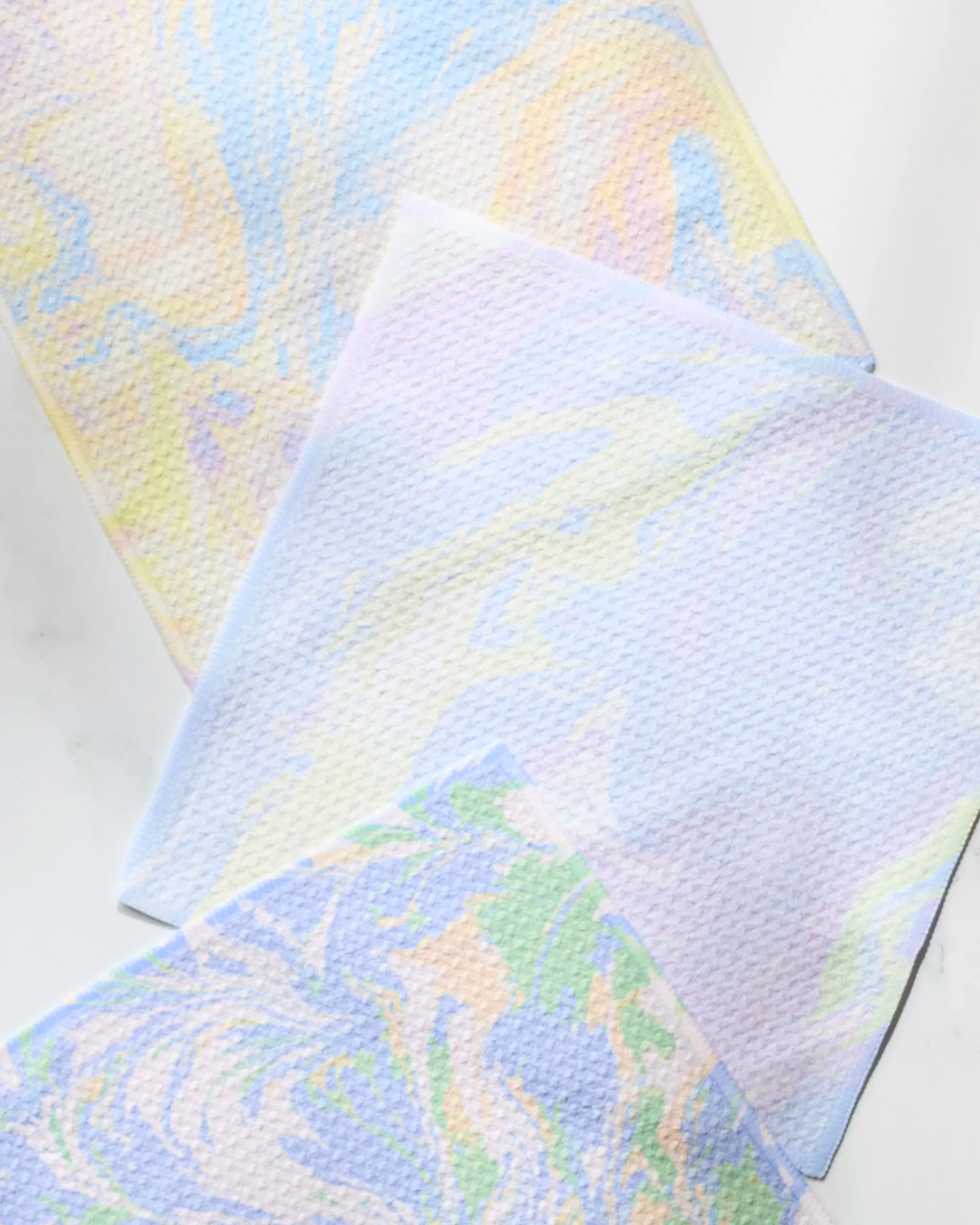 Geometry’s Dream Skies set features three eco-friendly dishcloths made from recycled materials, each with a pastel marbled pattern in blue, yellow, pink, and green arranged overlapping on a white surface.
