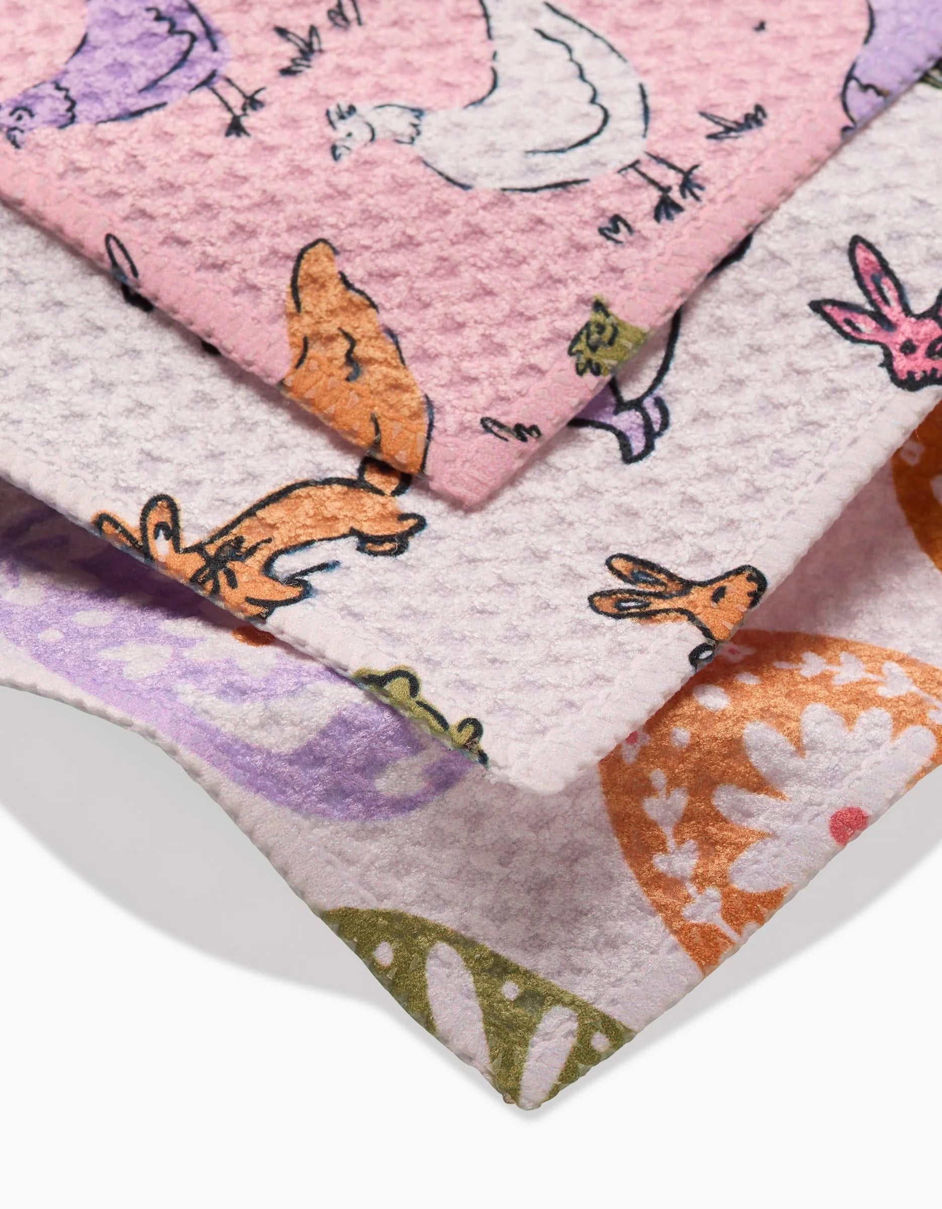 Three Kayla Ann Easter Eggs dishcloths stacked diagonally, made from Geoweave fabric and adorned with colorful animal and floral patterns—chickens, rabbits, and flowers—in soft pastel shades of pink, orange, purple, and green.