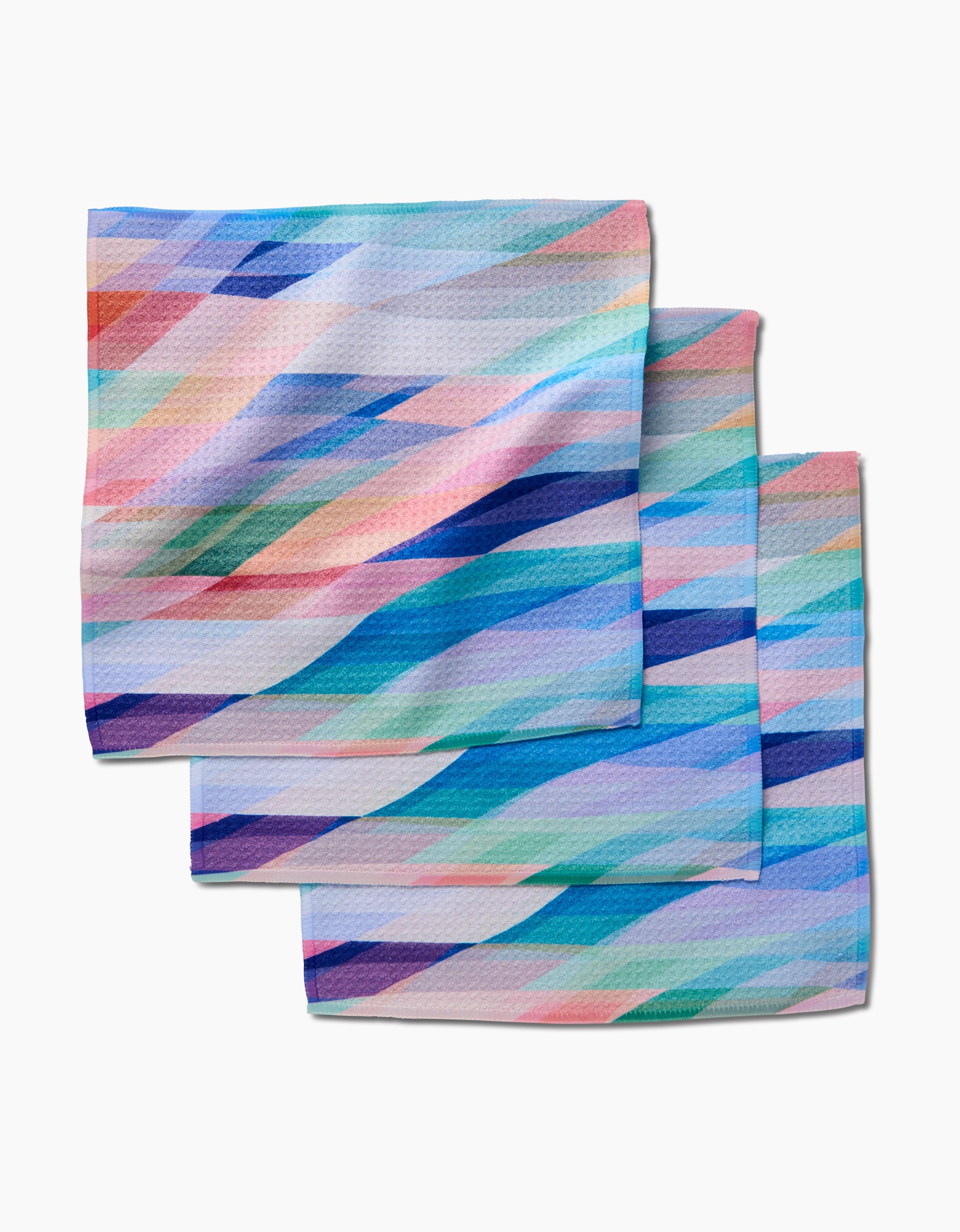 Rachel Parker’s Eventide features three square dishcloths made from recycled materials, each with vibrant diagonal stripes in pastel blue, pink, purple, and green, shown stacked on a white background.
