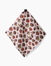 The Kayla Ann Fall Abundance dishcloth, crafted from Geoweave fabric, showcases brown, red, and green acorns and leaves on a light background and hangs from a black loop against a white surface.