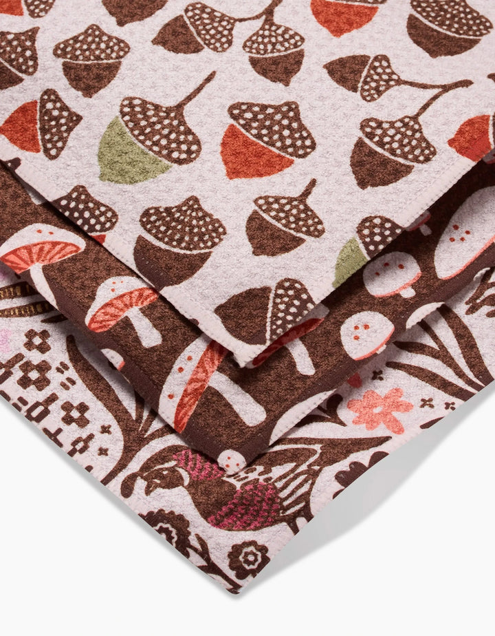 Kayla Ann’s Fall Abundance features three stacked Geoweave dishcloths with acorn, mushroom, and foliage patterns in earthy browns, reds, greens, and cream—stylish and eco-friendly, made from recycled materials.