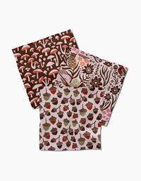 Kayla Ann’s Fall Abundance set includes three folded cloth napkins made from recycled materials, featuring brown mushrooms, flowers and leaves, and acorns on a white background.