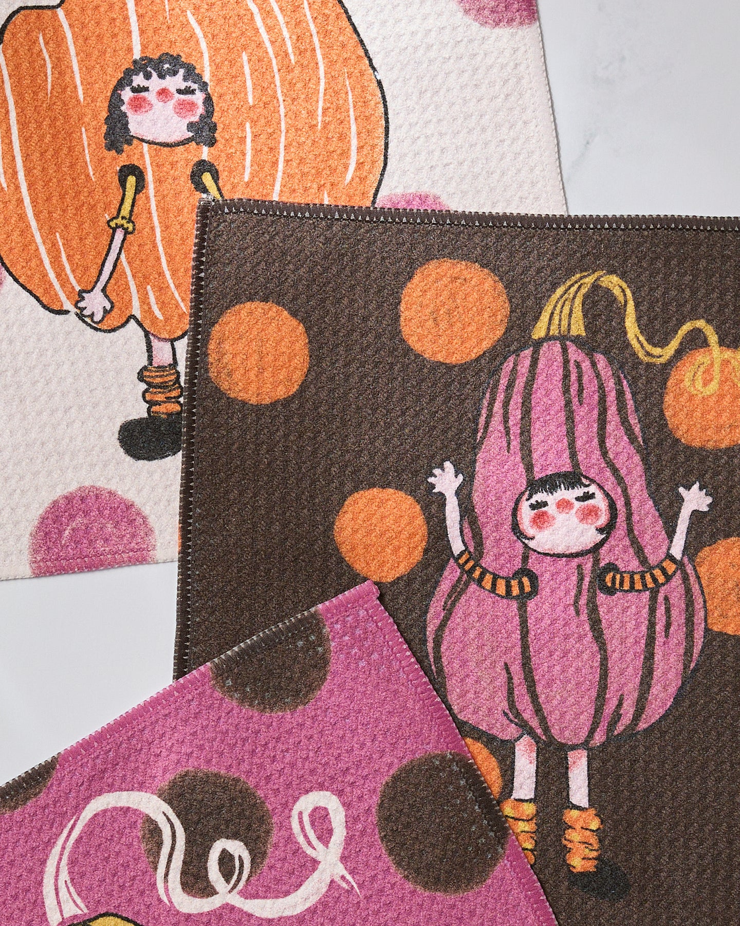 Geometry’s Fall Day Parade features three vibrant, eco-friendly fabric pieces with playful pumpkin-costumed girls and cheerful polka dots in warm fall shades.