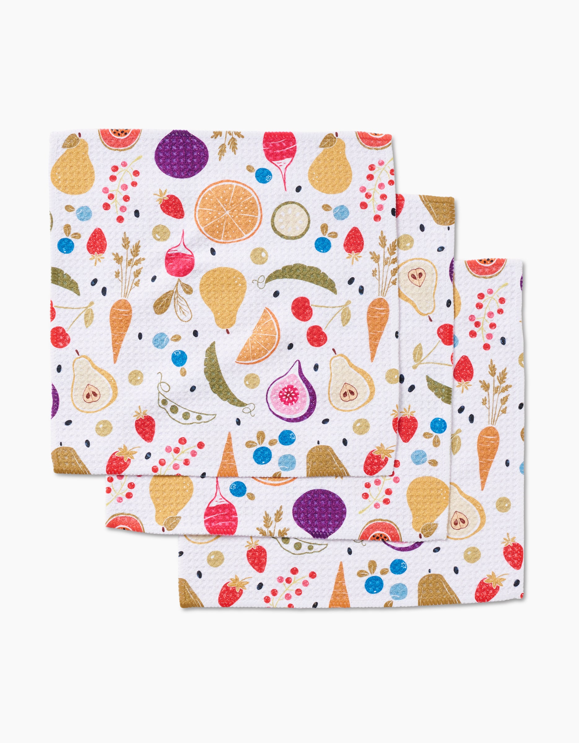 Three white Sara Mari Farmers Market Geoweave dishcloths, featuring colorful carrots, figs, oranges, berries, peas, and pears patterns, are overlapped on a white background.