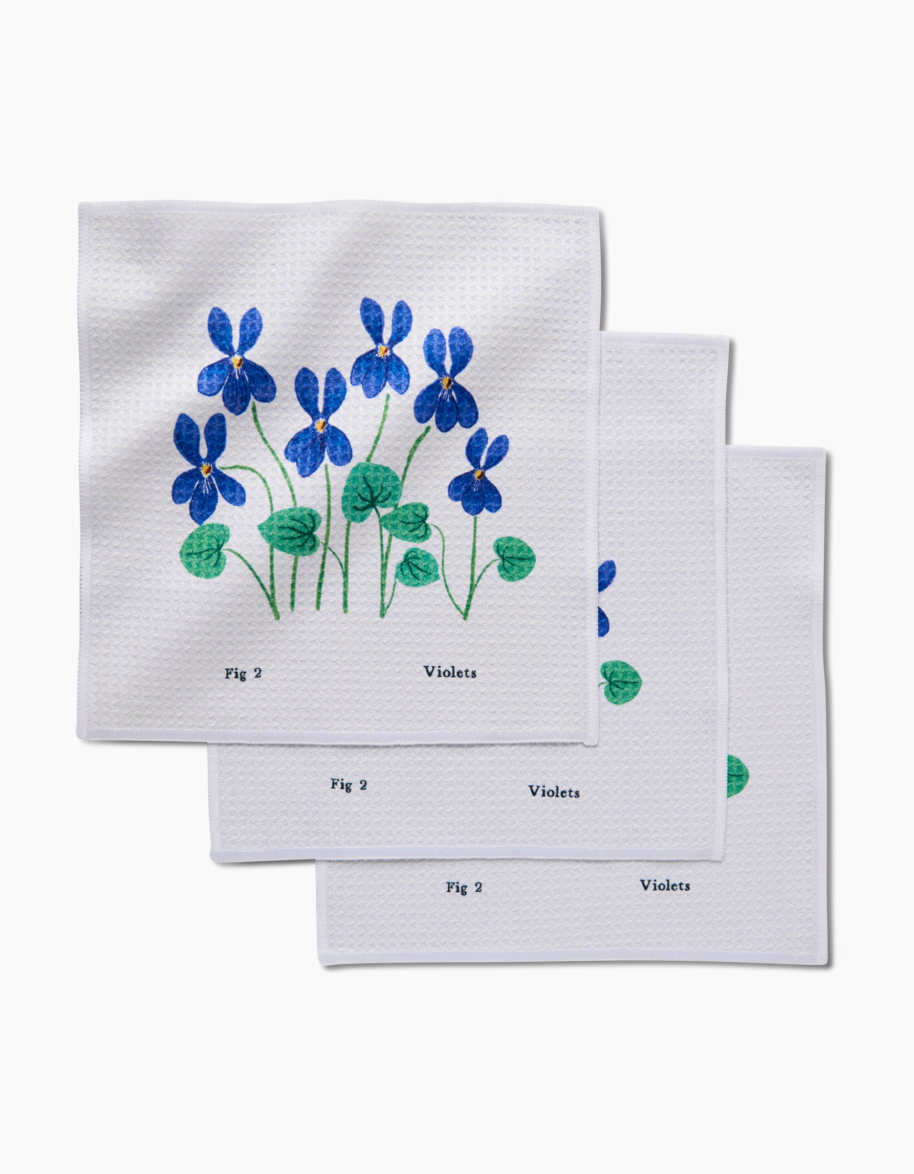 The February Violets dishcloth set by Linda Fox includes three white Geoweave cloths, each featuring blue violet flowers with green stems, Fig 2 and Violets printed below the design.