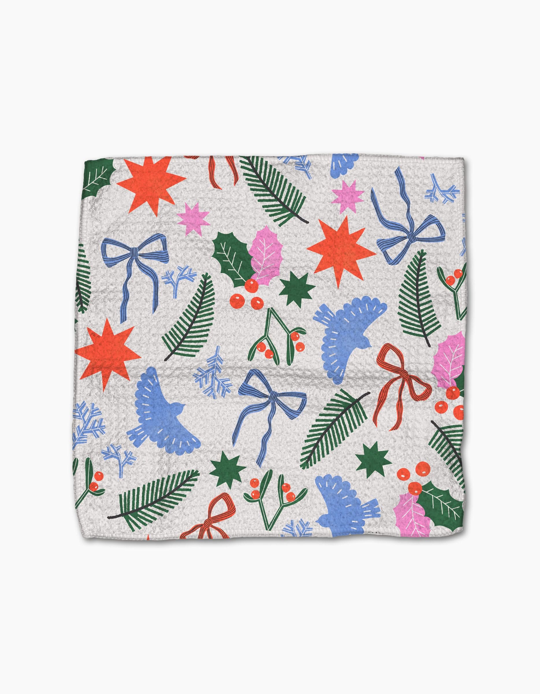 The Claire Iglesias Festive Cheer dishcloth set is made from recycled materials and showcases red stars, blue bows, green pine branches, holly leaves, mistletoe, and snowflakes on a light background.