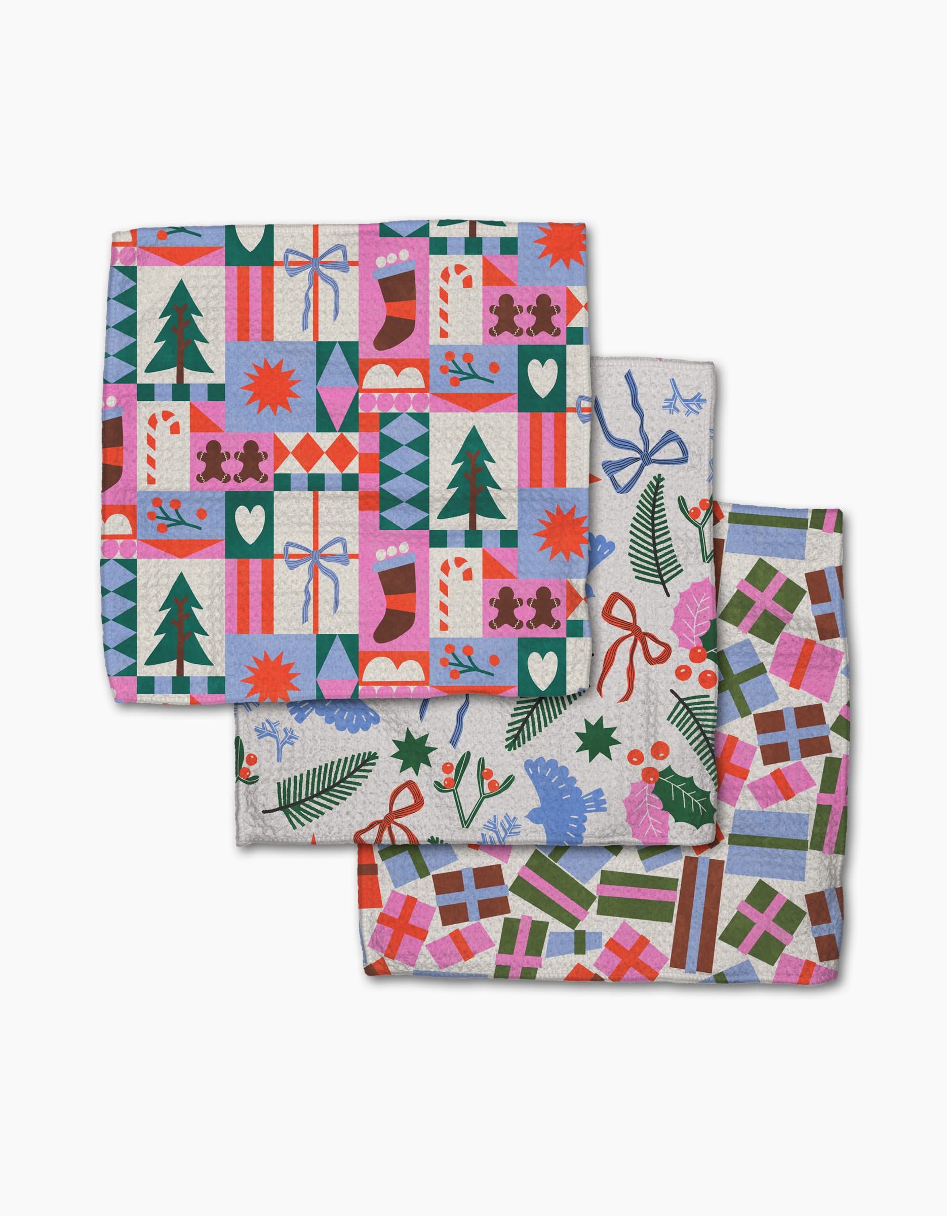 The Claire Iglesias Festive Cheer set features three folded napkins with holiday designs—gifts, candy canes, stockings, trees, stars, and snowflakes on white—crafted from recycled materials for an eco-friendly celebration.