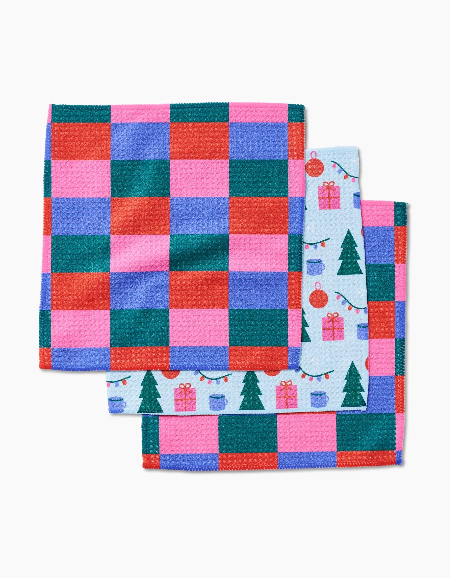Laura Supnik’s Festive Doodles features three folded dishcloths: two with red, green, pink, and blue checks, and one with a festive print of Christmas trees and ornaments on light blue. Made from recycled materials.
