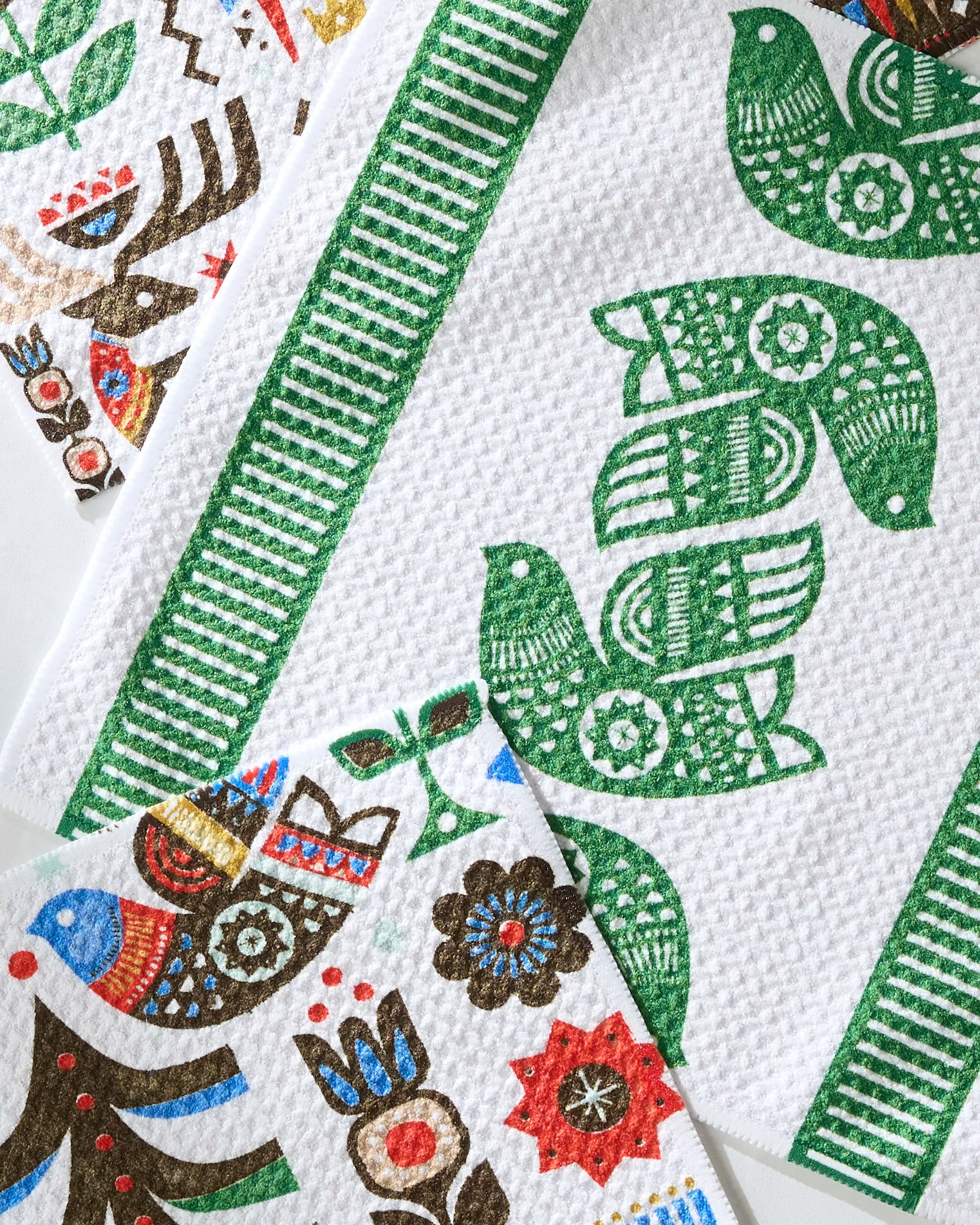 Geometry’s Festive Folk dishtowels feature super-absorbent fabric and vibrant folk art birds, flowers, and patterns in green, blue, red, brown, and gold—arranged in colorful borders and clusters for a decorative touch.